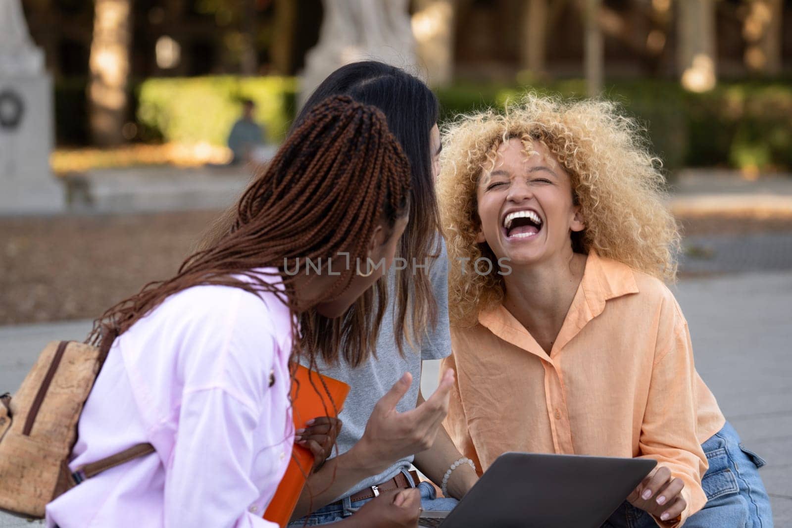 Three multi ethnic students enjoying time together after university class laughing with positive mood in the campus by papatonic