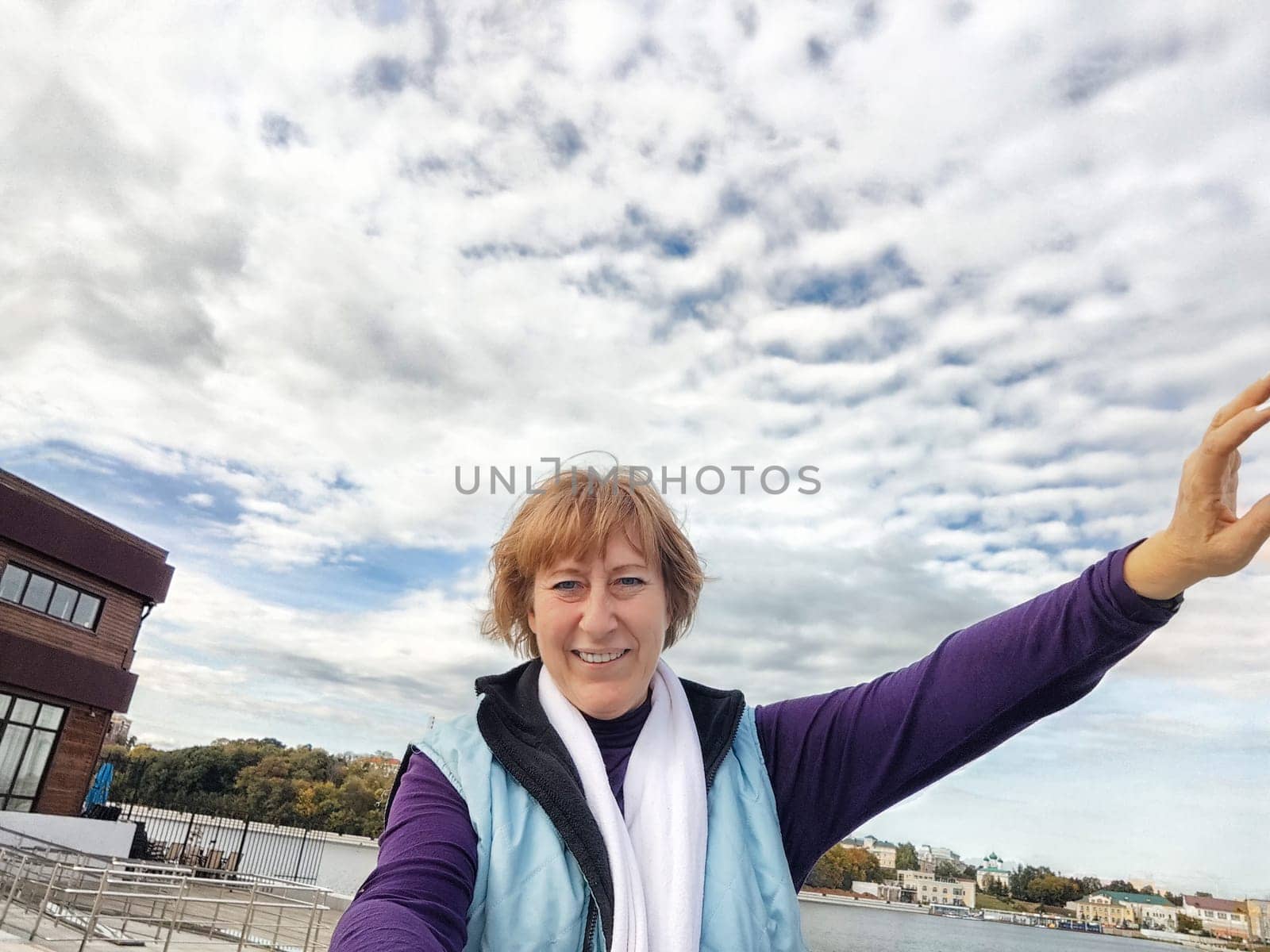 Relaxed mature caucasian female looking at camera and making selfie outside. Positive senior woman against city street background. Adult middle agged girl Blogger posing and taking photo for the internet