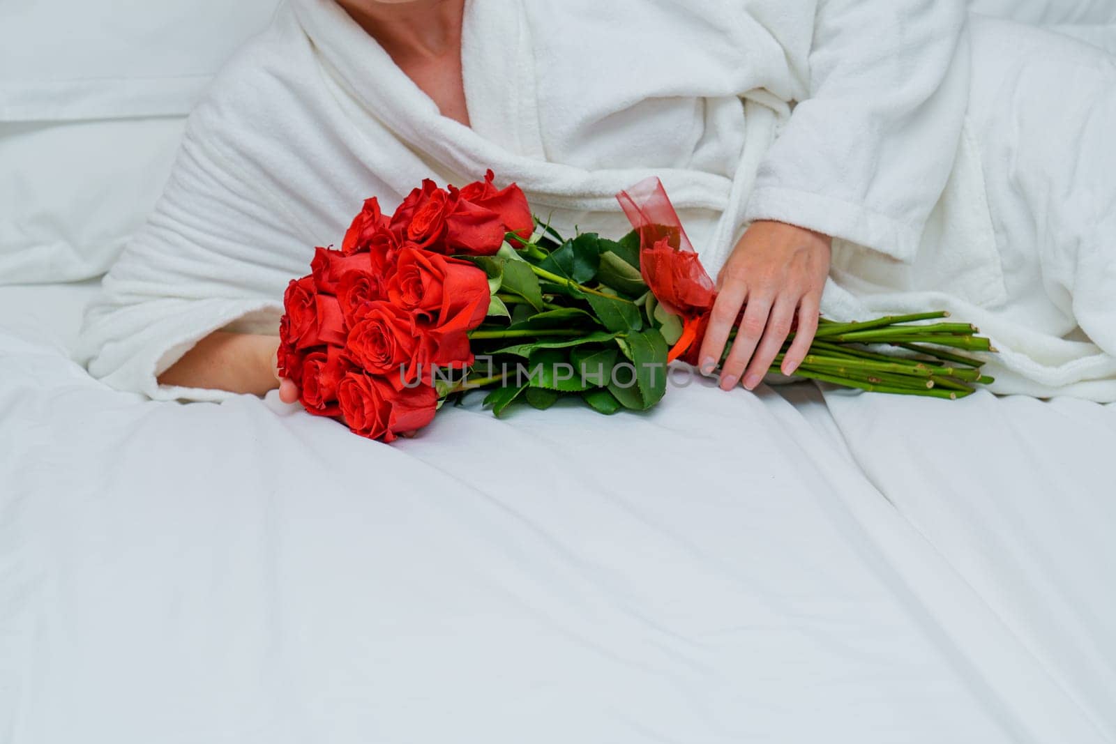 An elegant and luxurious scene of a beautiful woman reclining on a plush hotel bed, surrounded by a large bouquet of vibrant red roses, exuding a sense of relaxation and indulgence.