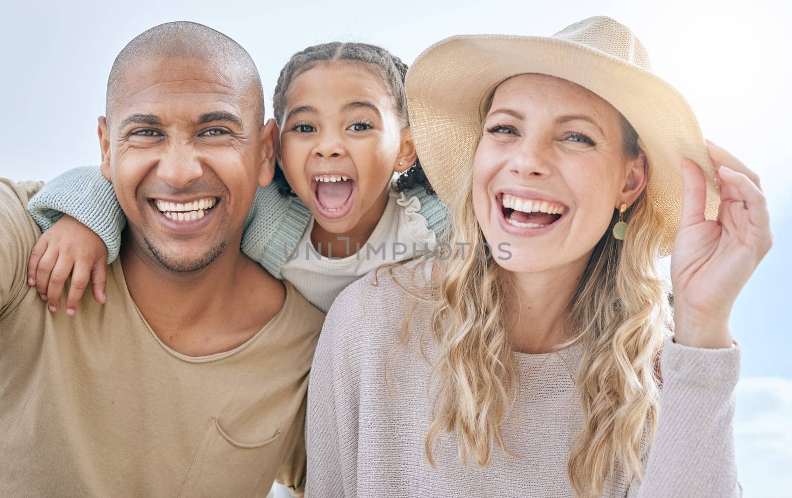 Summer, blue sky and portrait of young family having fun, laugh and play together. Multicultural mom, dad and girl outdoors on beach holiday and vacation. Love, bonding and couple with kid on weekend by YuriArcurs