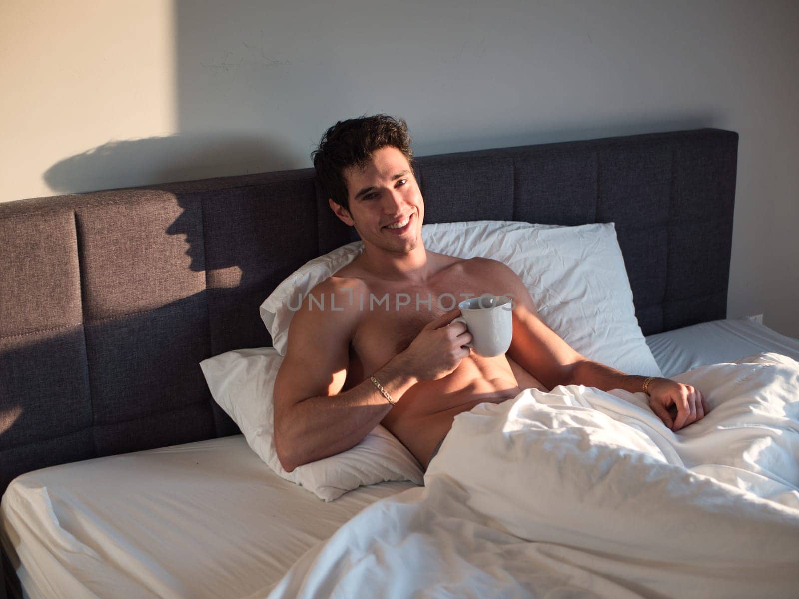 Photo of a shirtless man enjoying a peaceful morning in bed with a cup of coffee by artofphoto