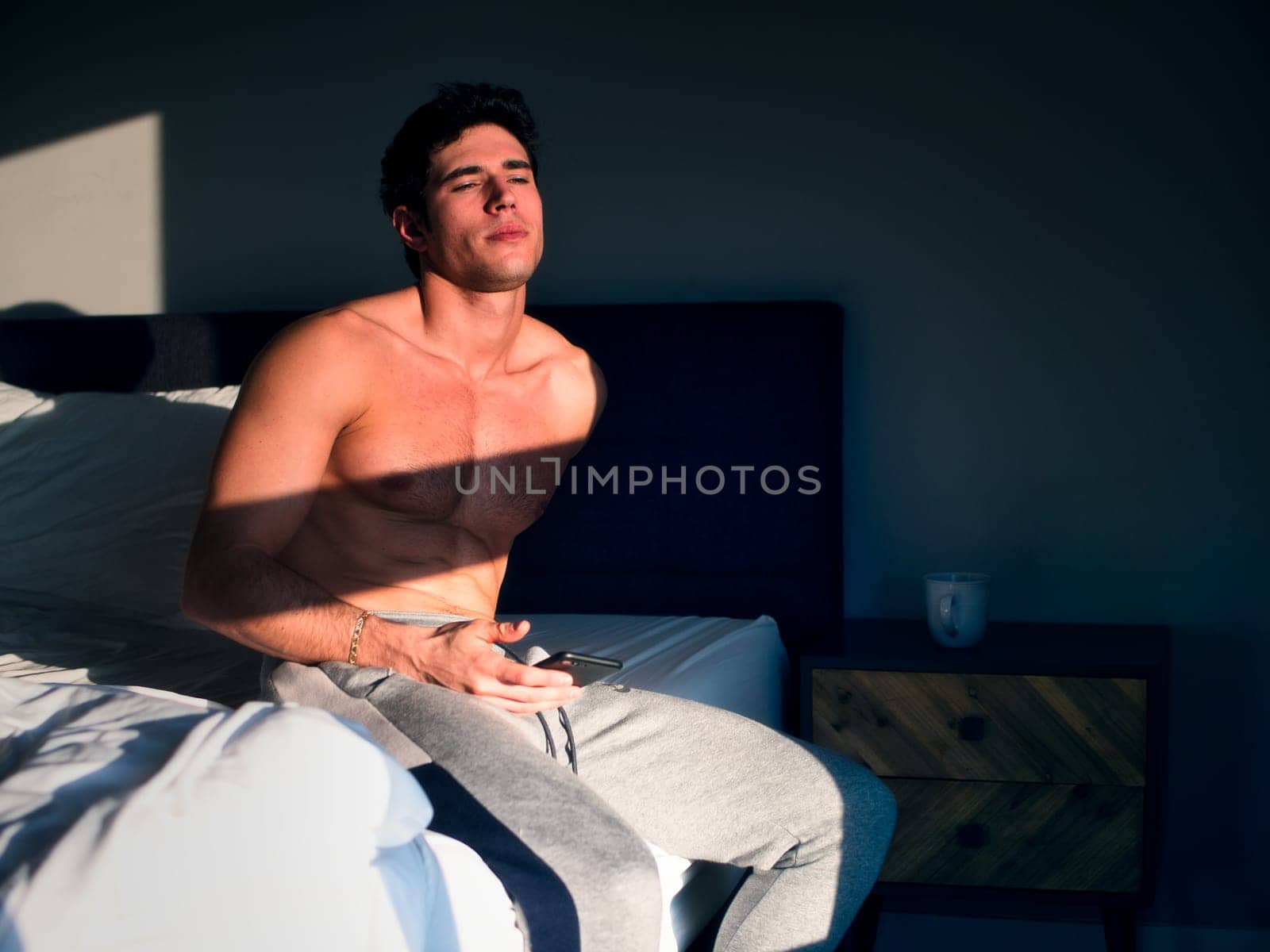 Photo of a shirtless man sitting on a bed in a bedroom in the morning by artofphoto