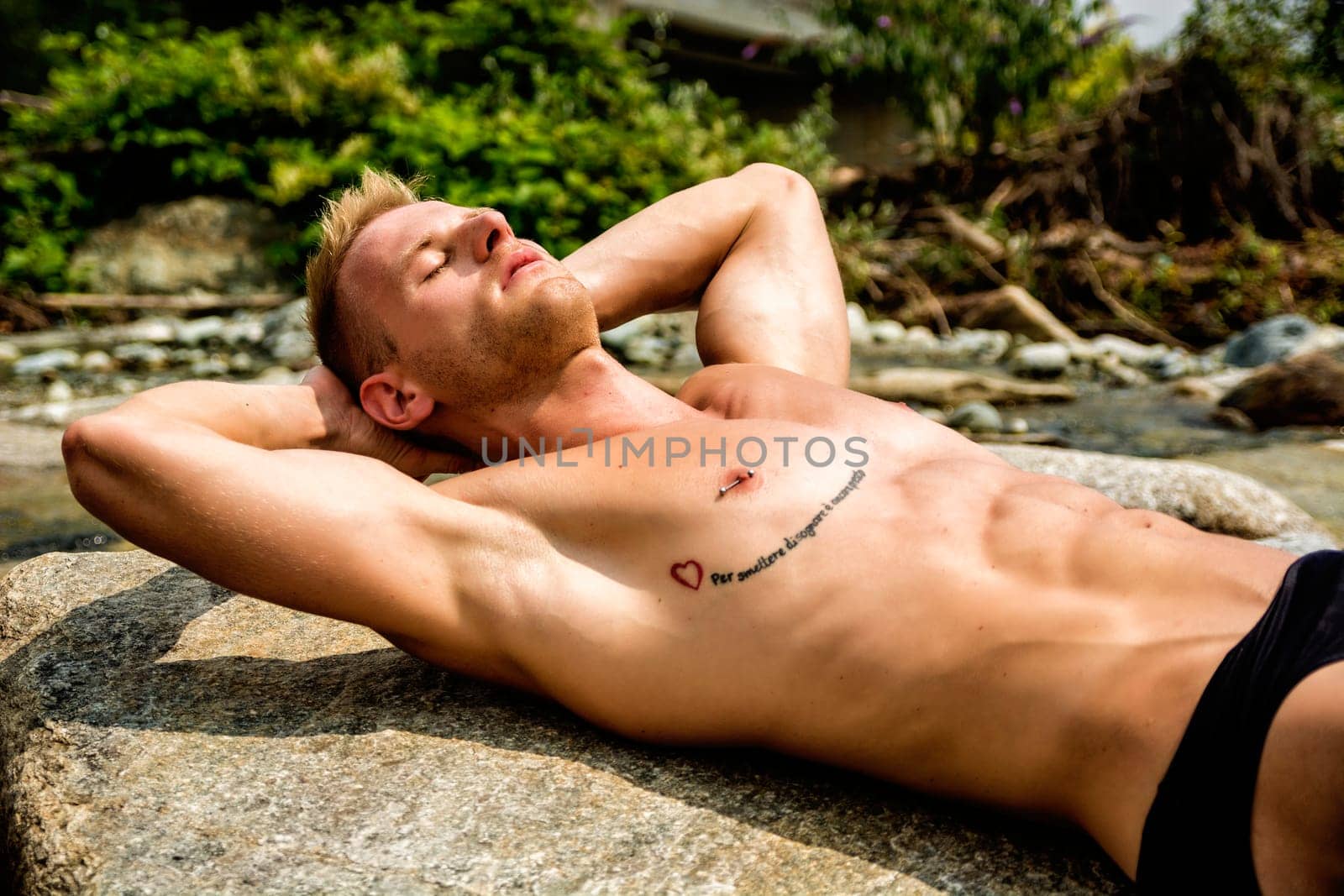 A man laying on top of a rock next to a river