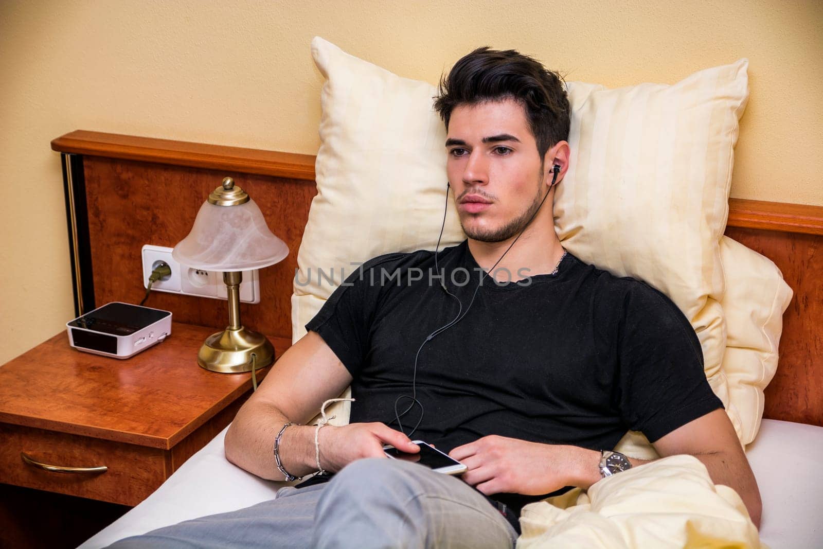 Photo of a young man enjoying music in bed by artofphoto