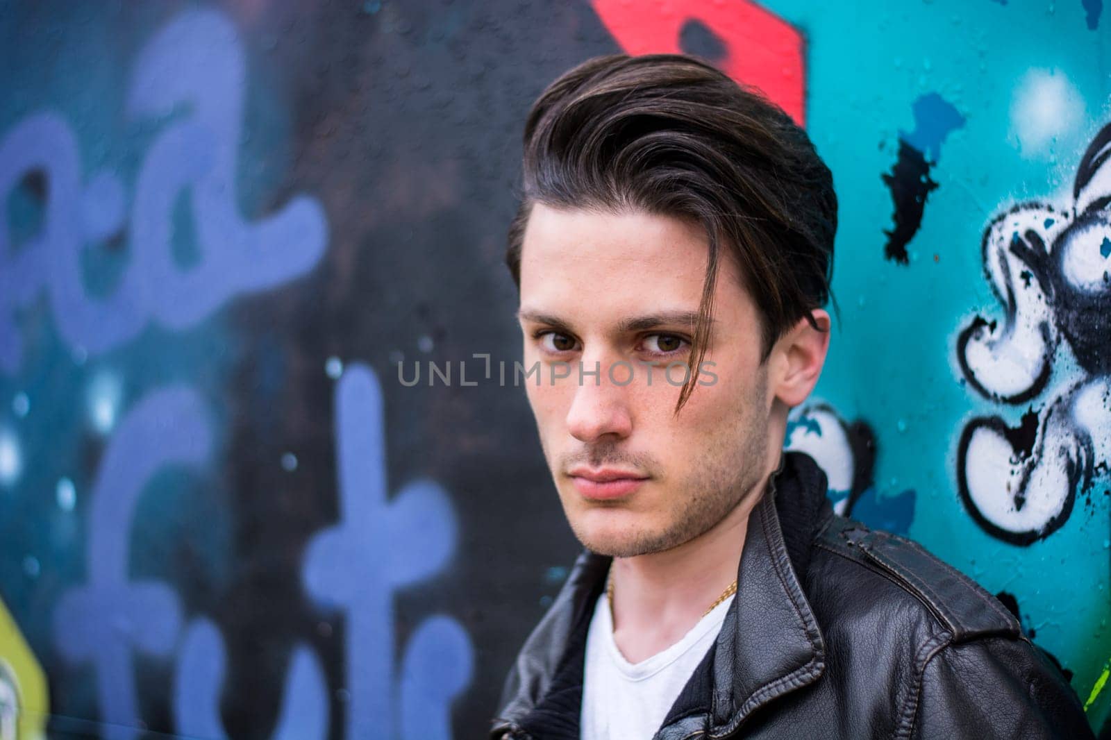 Photo of a man posing in front of a vibrant graffiti wall wearing a stylish leather jacket by artofphoto