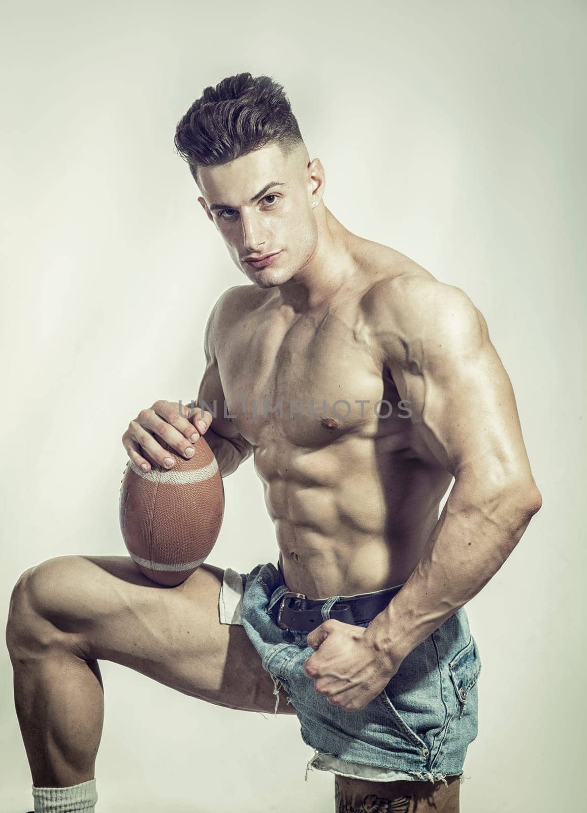 Photo of a muscular man with a football, striking a pose in a professional studio setting by artofphoto