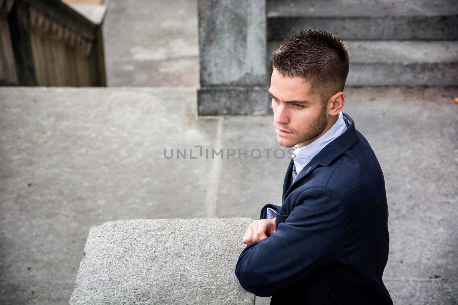 A man in a suit leaning against a stone wall
