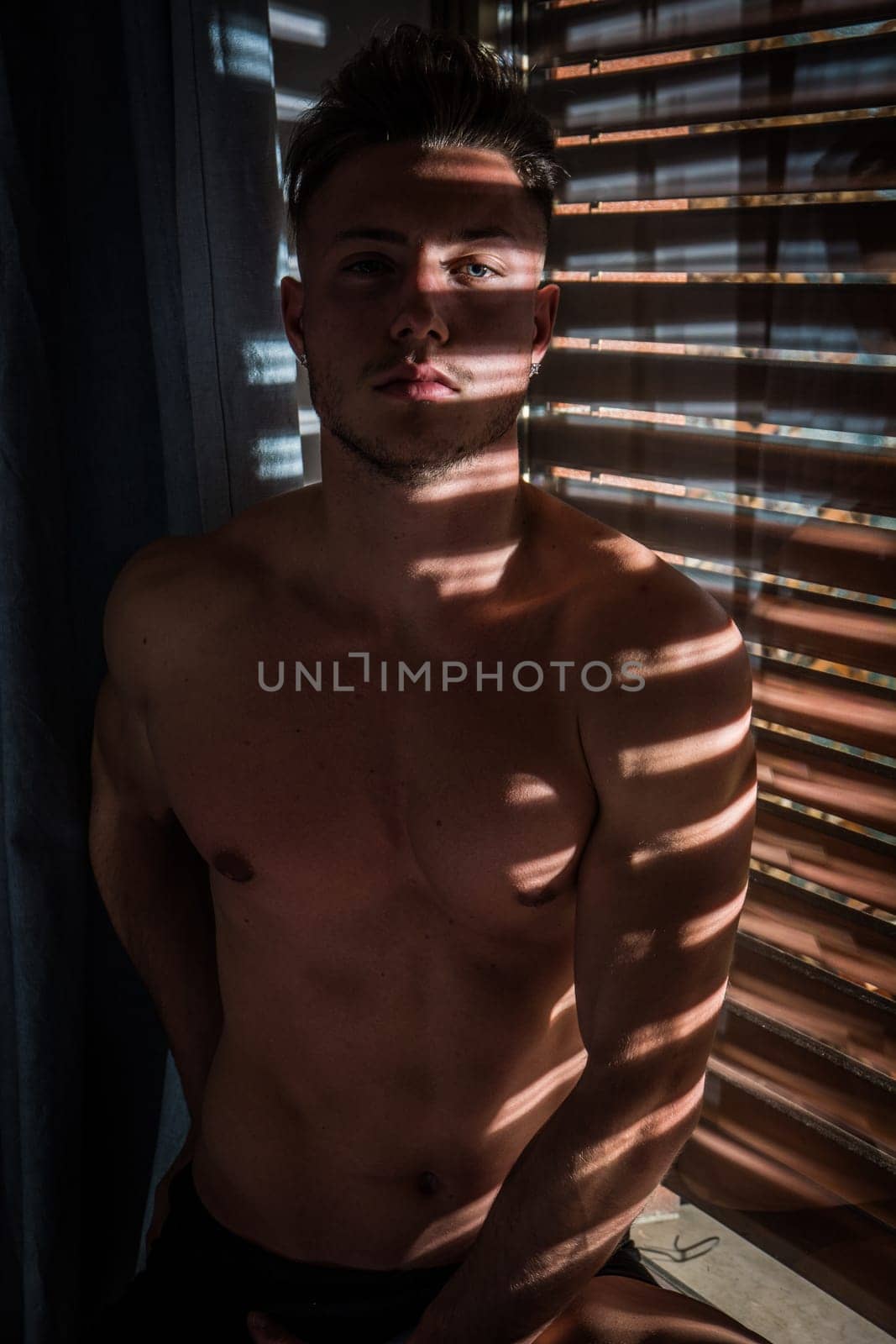 Photo of a shirtless man sitting in front of a window by artofphoto
