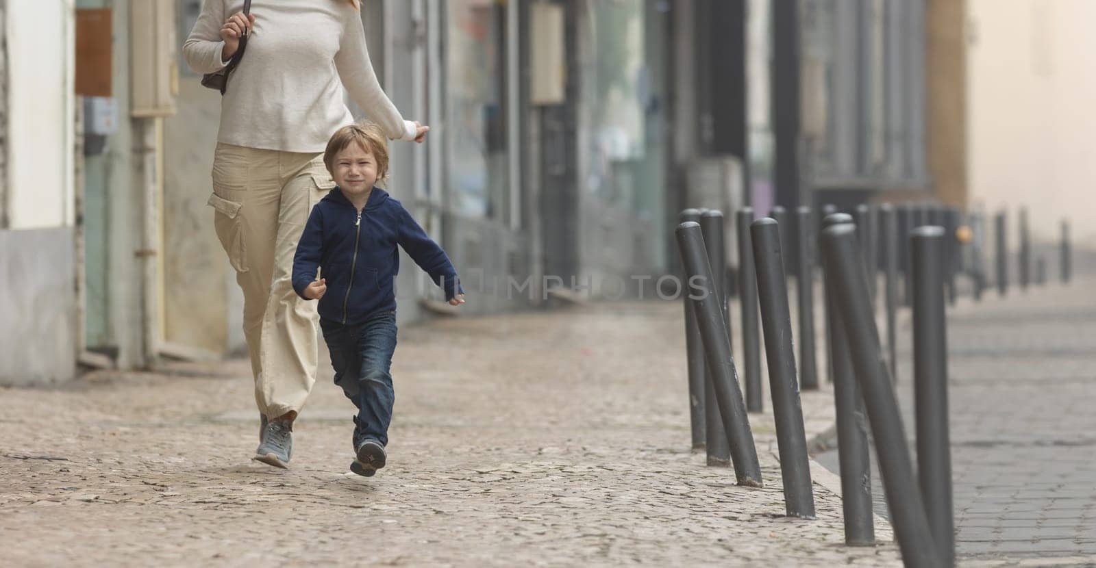 A woman and a child running down a street - telephoto