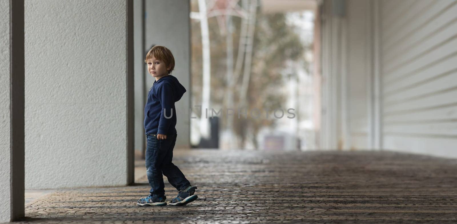 A young boy walking down a sidewalk next to a building - telephoto