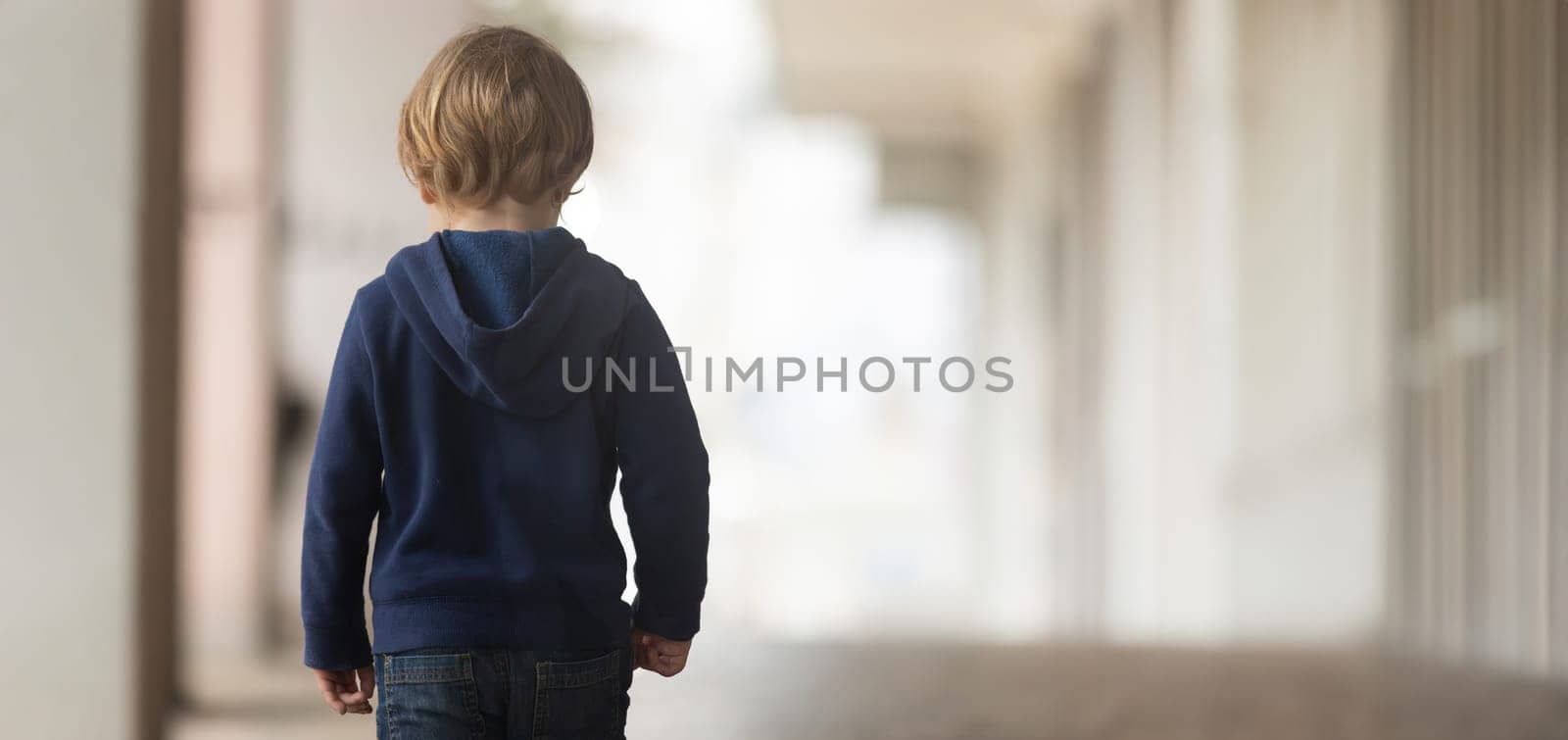 A young boy walking down a hallway in a blue sweater