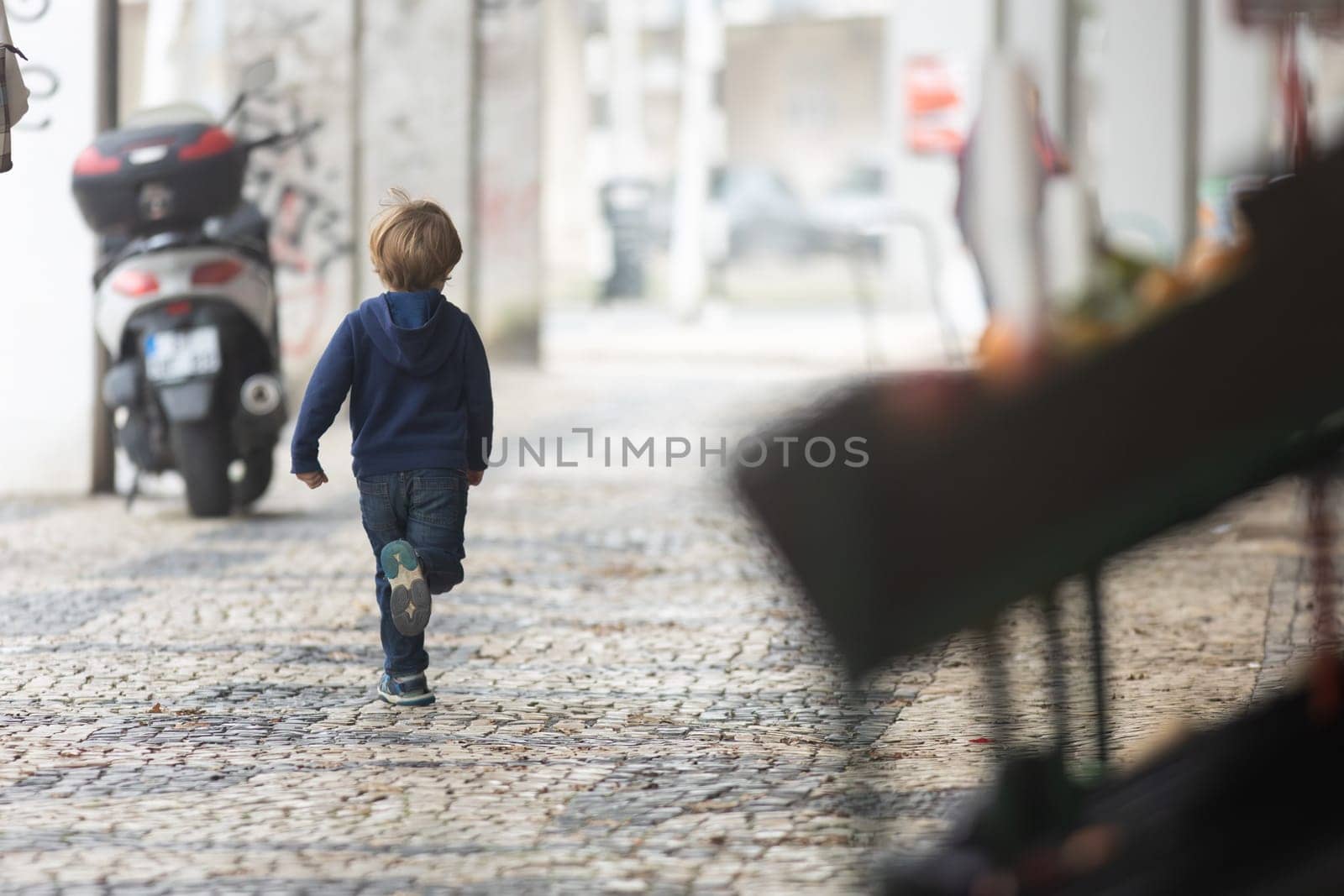 A young boy walking down a cobblestone street - view from behind