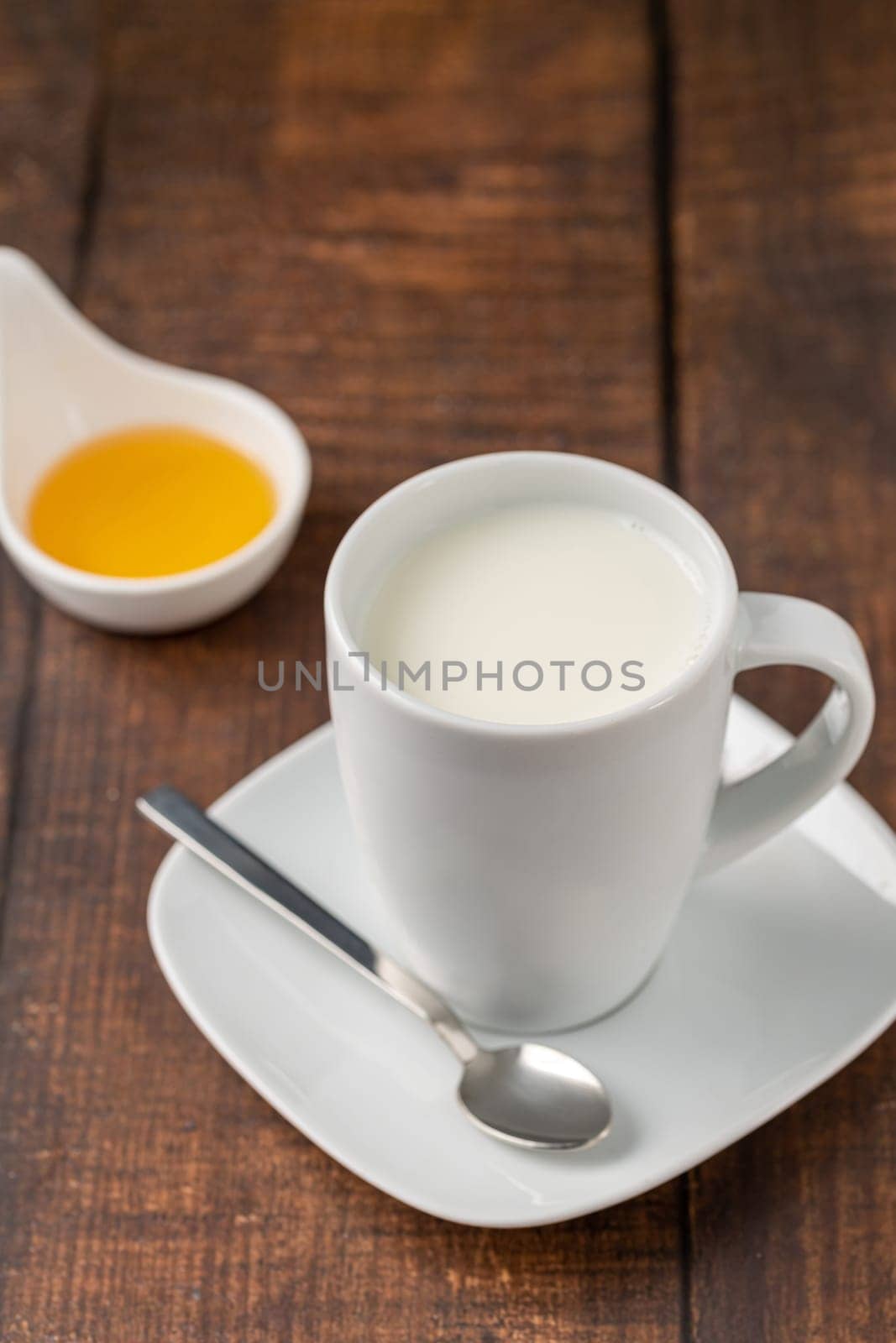 Milk in a porcelain cup and honey in a porcelain bowl on a wooden table by Sonat