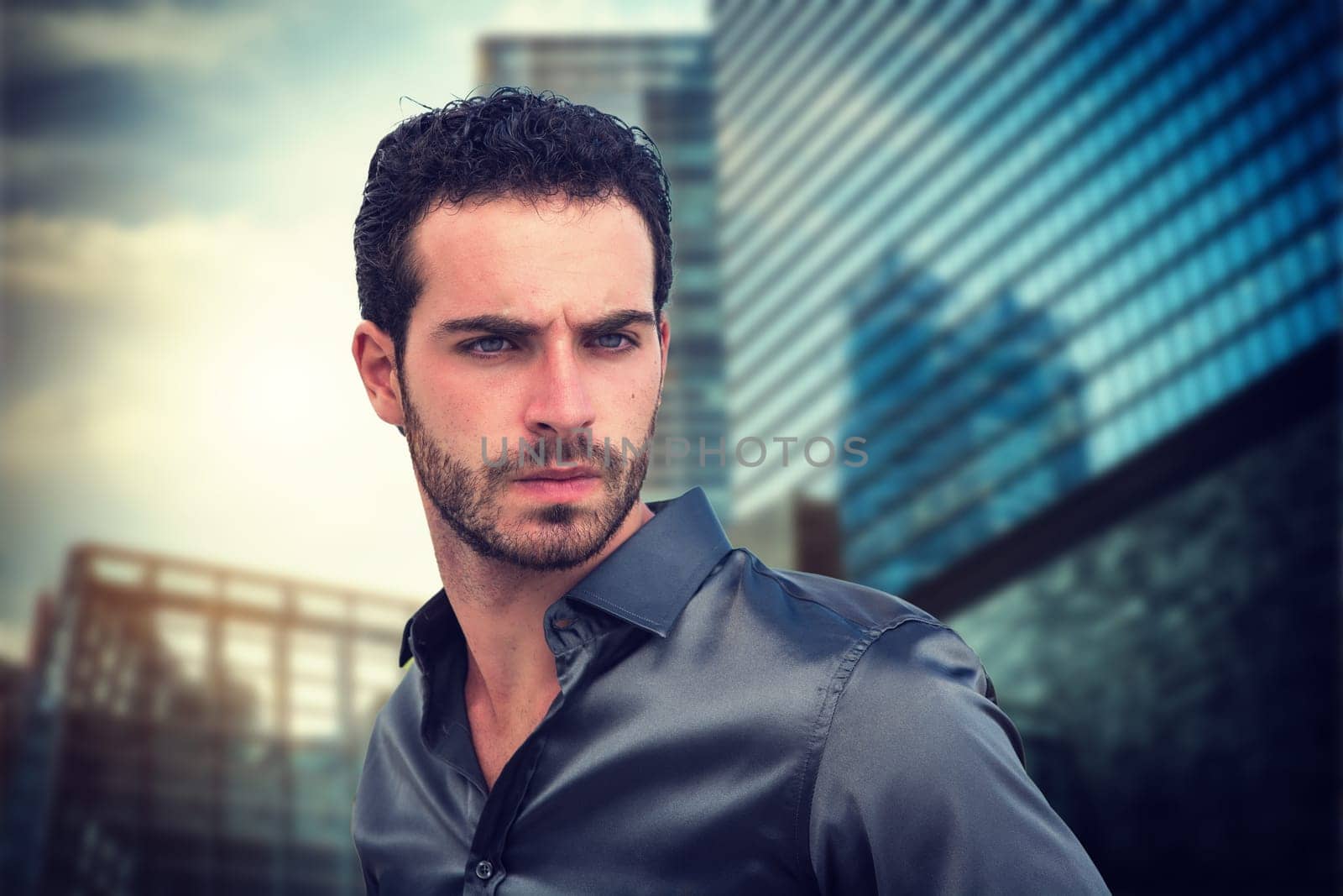 A young handsome man standing in front of a tall building in a modern city. A Glimpse of Urban Majesty: A Man Standing in Front of a Tall Building