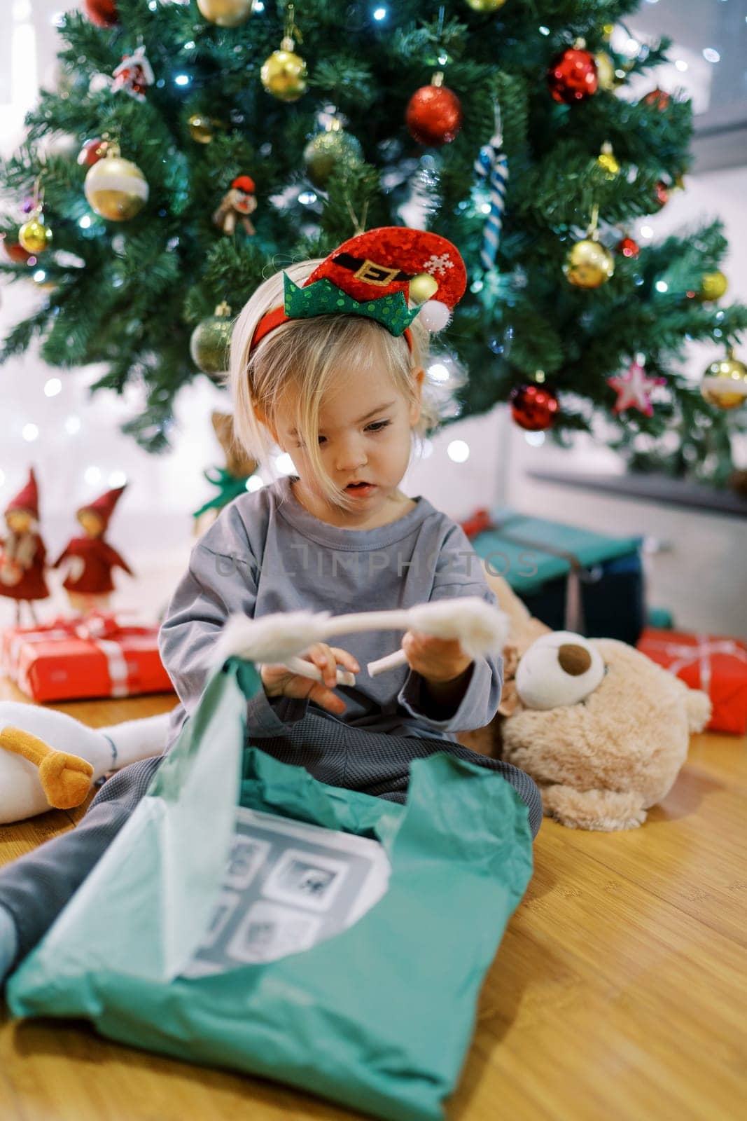 Little girl in a hoop with a gnome hat examines a hoop with cat ears, sitting by the Christmas tree. High quality photo