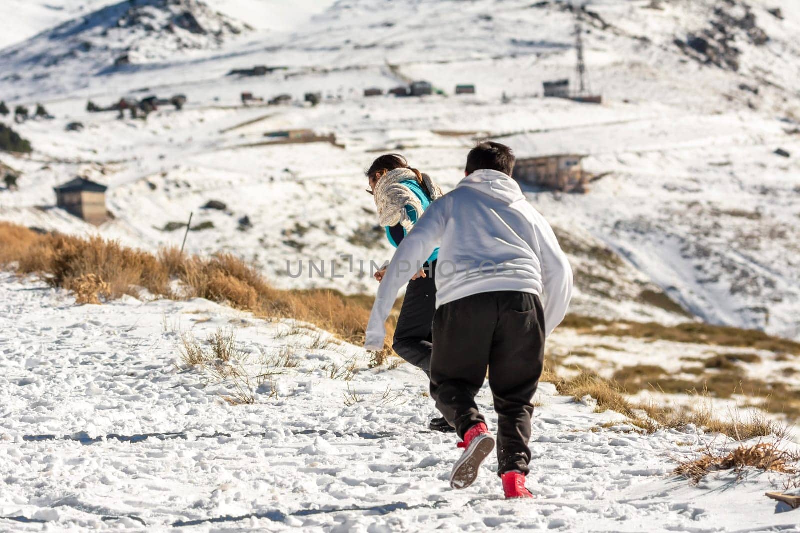 Latin mother and son running in the snow in Sierra Nevada Granada, Andalusia Spain