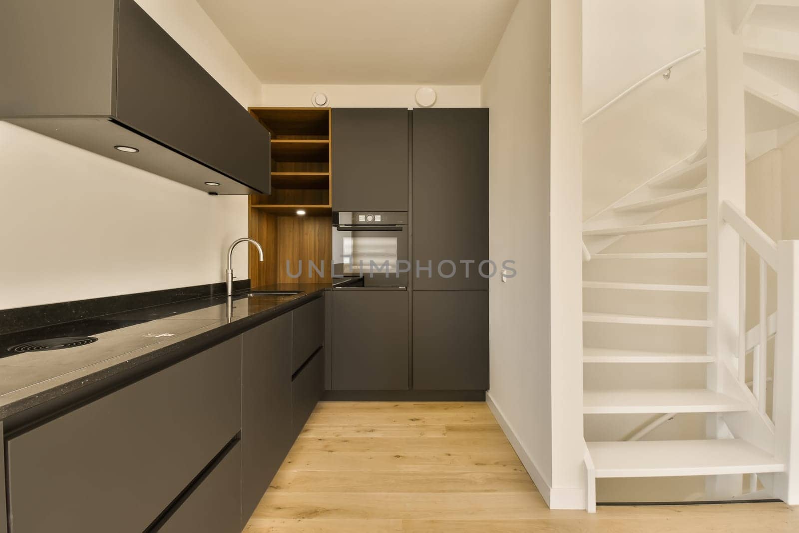 a modern kitchen and staircase in a house with white walls, wood flooring and dark grey cabinetd cupboards