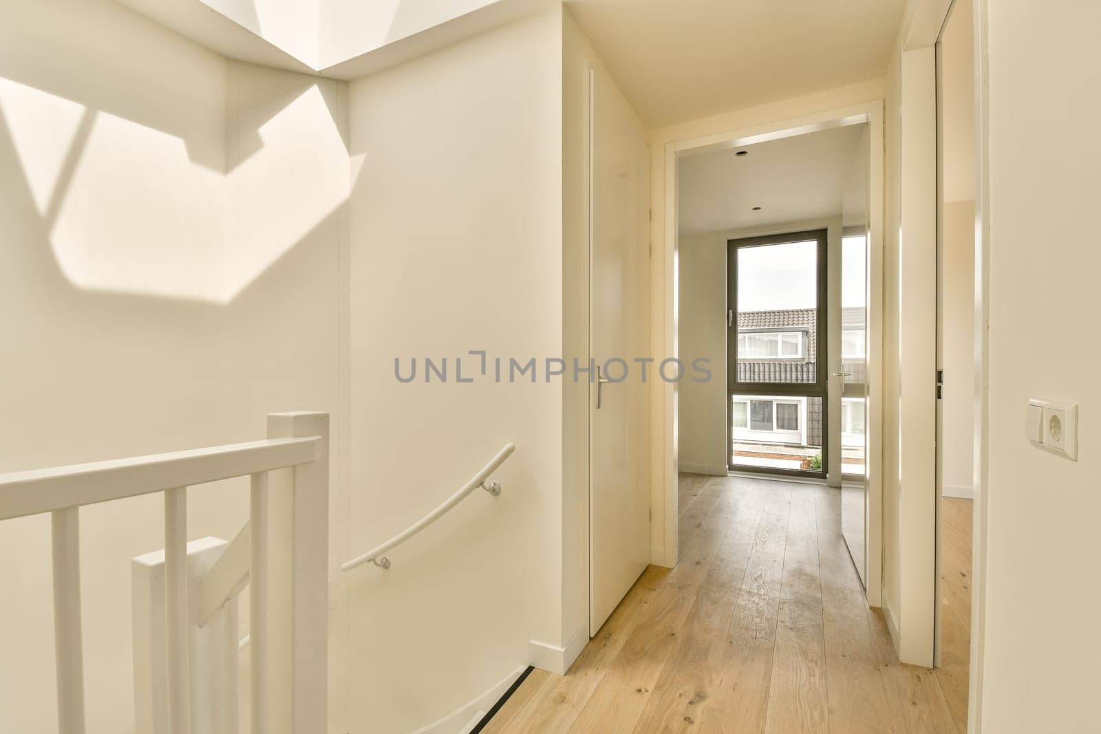 an empty hallway with wood flooring and white trim on the walls, leading to a large open door that leads to a balcony