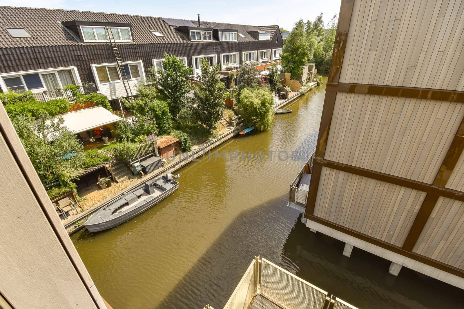 a canal with houses in the background and boats parked on the riverbanks, as seen from an apartment balcony