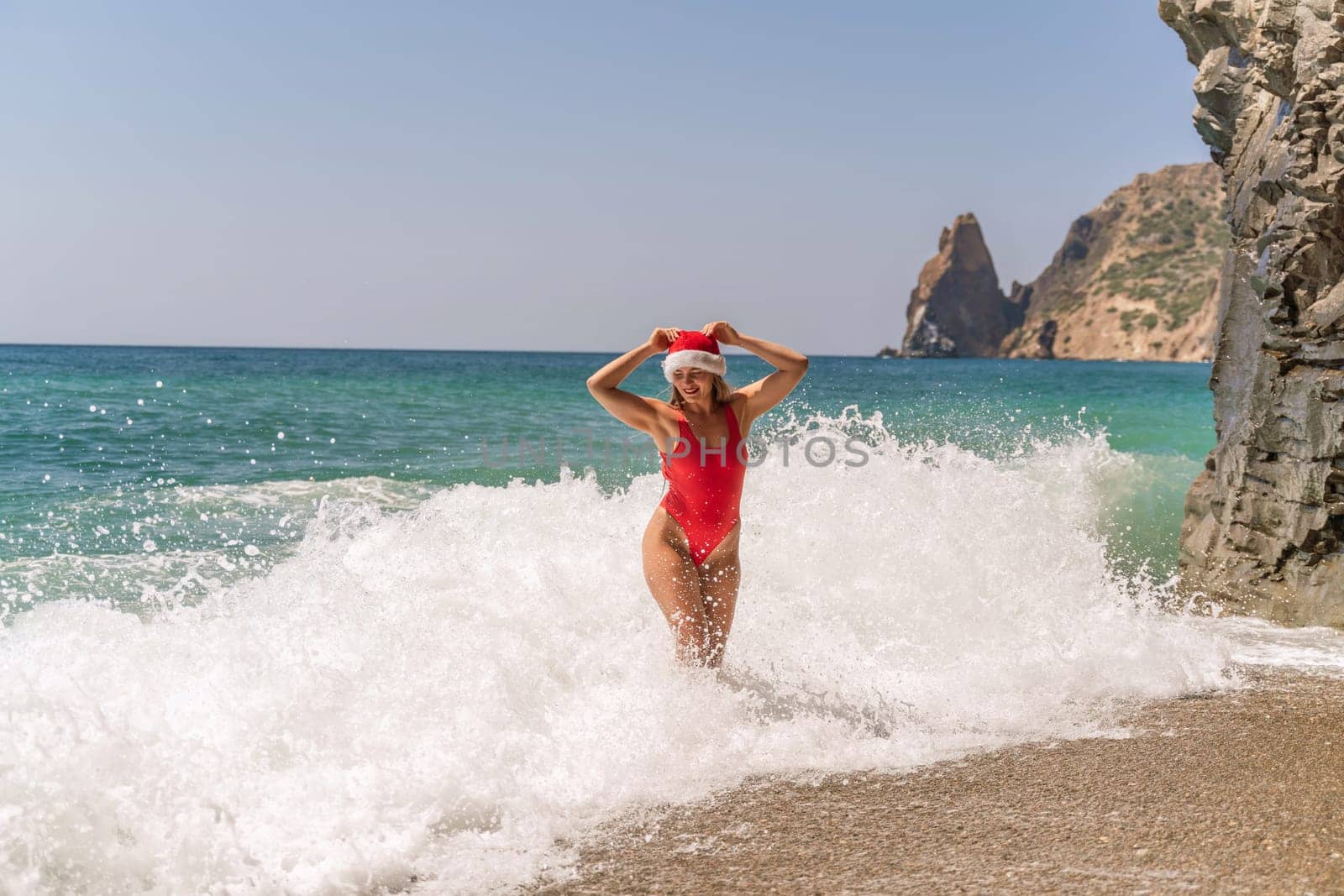 A woman in Santa hat on the seashore, dressed in a red swimsuit. New Year's celebration in a hot country