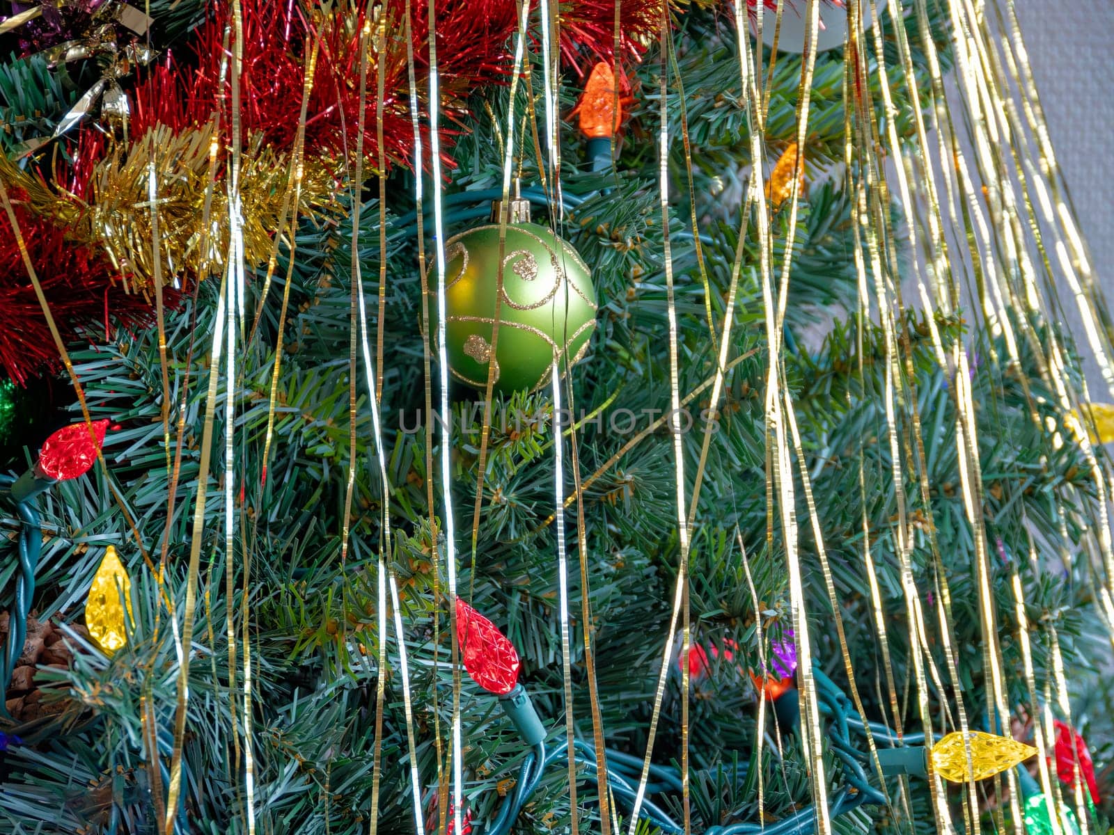 Green ornamental bauble with decorative lights among the chistmas tree brenches. Closeup look of xmas tree