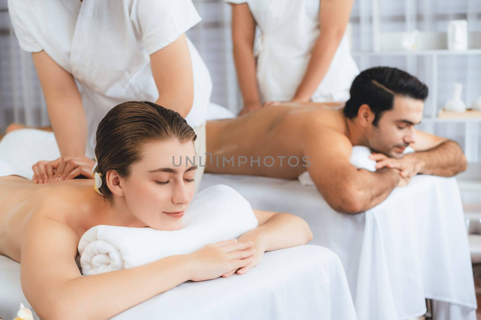 Caucasian couple customer enjoying relaxing anti-stress spa massage and pampering with beauty skin recreation leisure in day light ambient salon spa at luxury resort or hotel. Quiescent