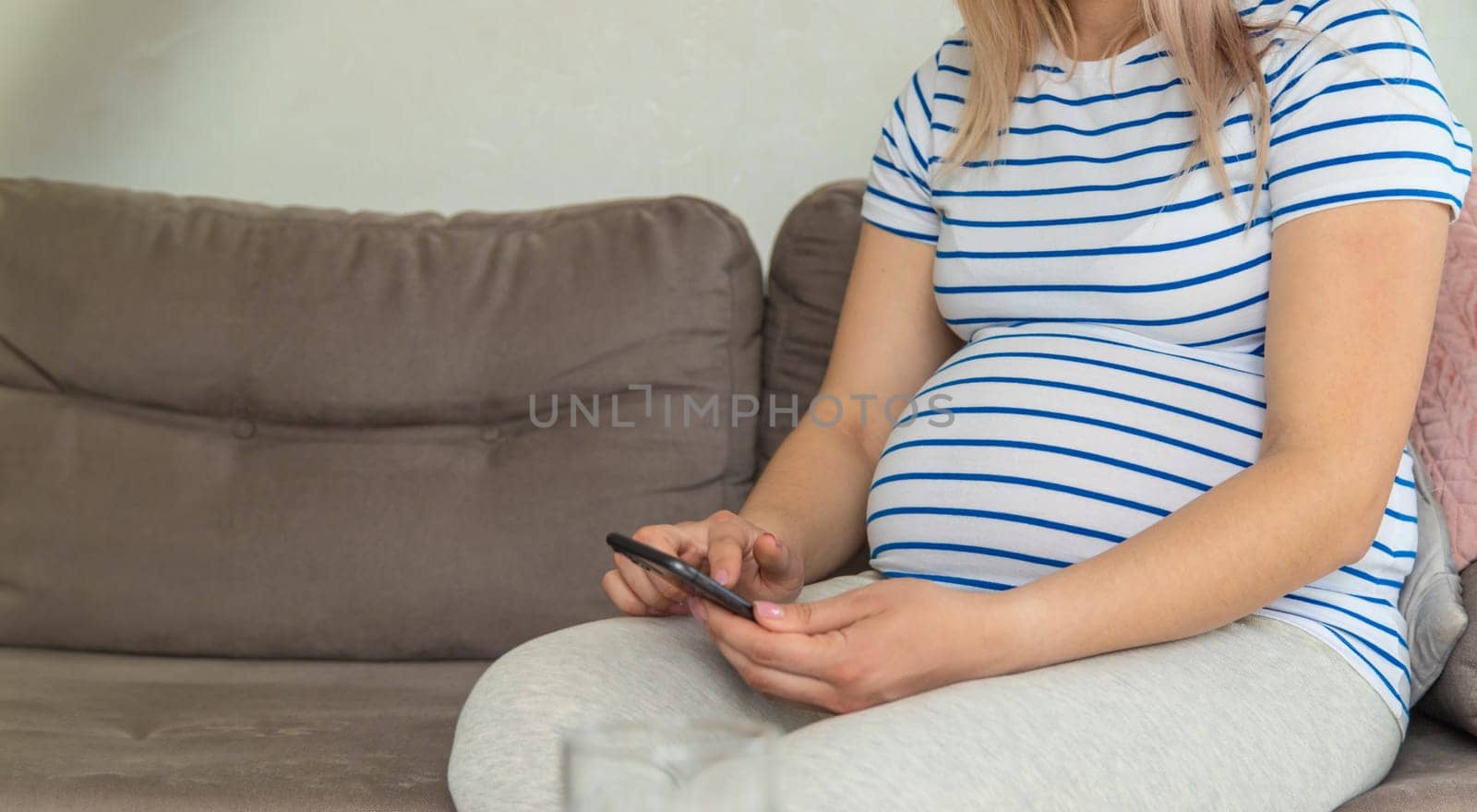 A pregnant woman plays on the phone on the Internet. Selective focus. Home.