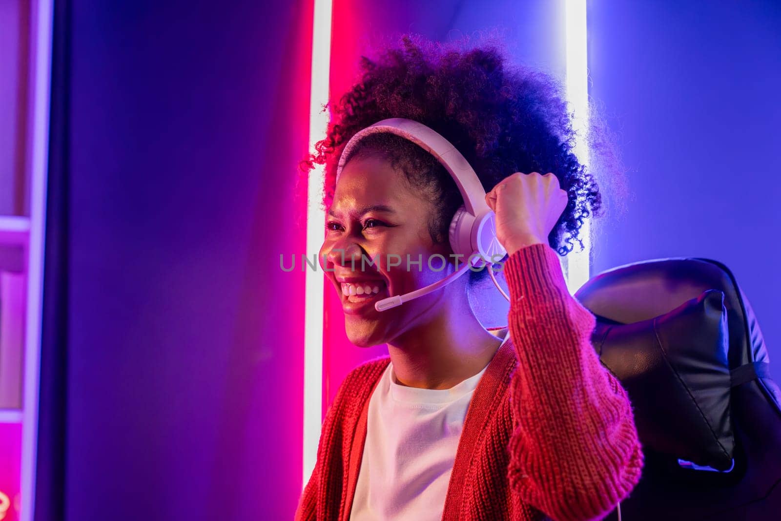 Gaming streamer, African girl playing online fighting with Esport skilled team wearing headphones in neon color lighting room. Talking other players planing strategies to win competitors. Tastemaker.