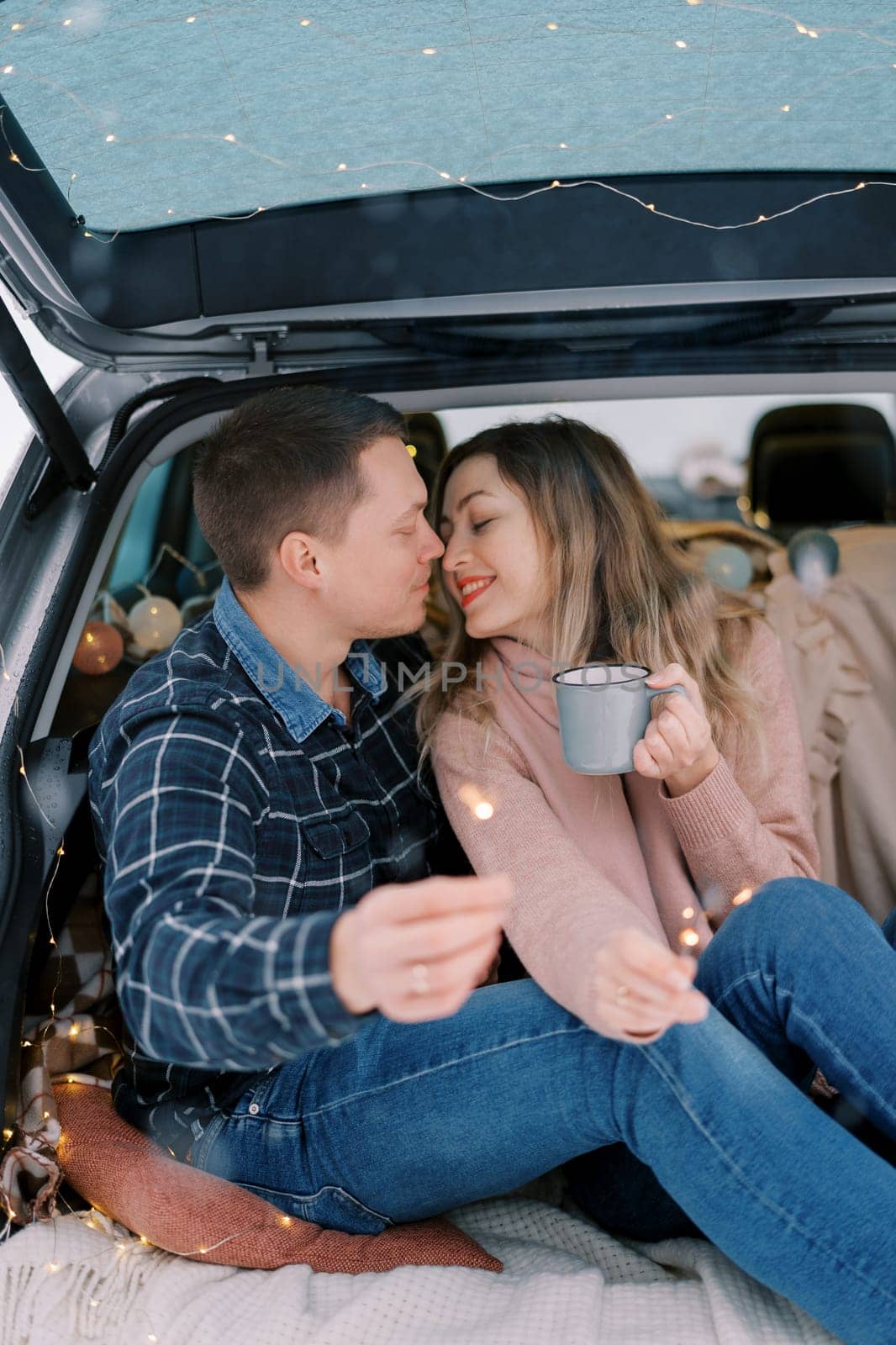 Young man and woman almost kiss while sitting with sparklers in their hands in the trunk of a car. High quality photo