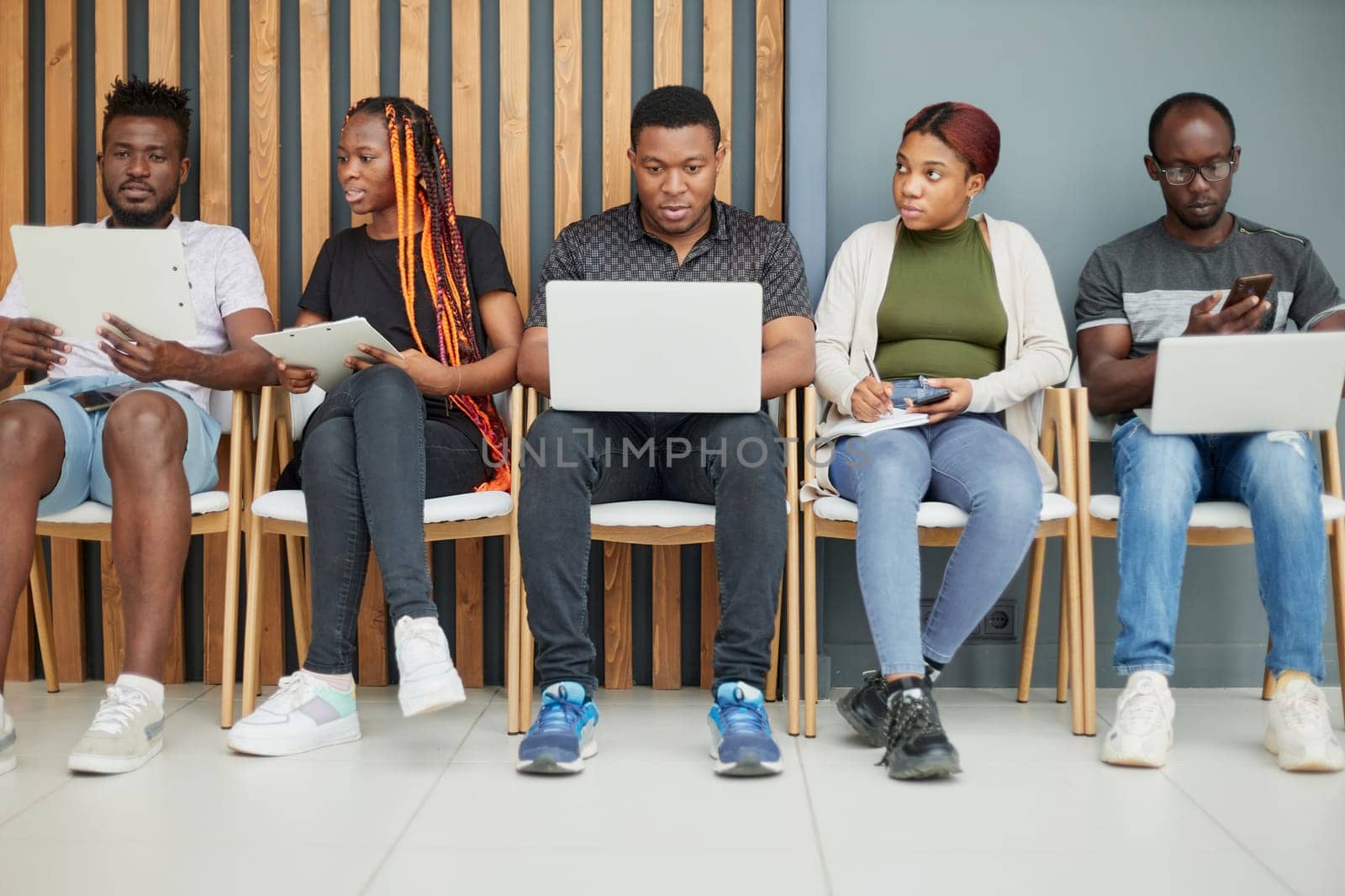 A group of candidates are being interviewed on a laptop while sitting on a chair in a conference room