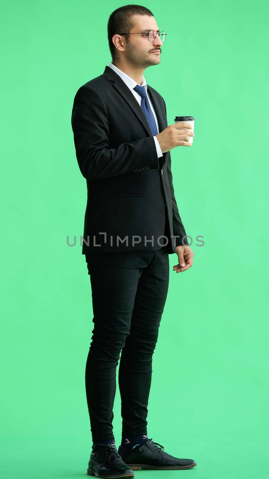 young man in full growth. isolated on green background. holding a mug of coffee by Prosto