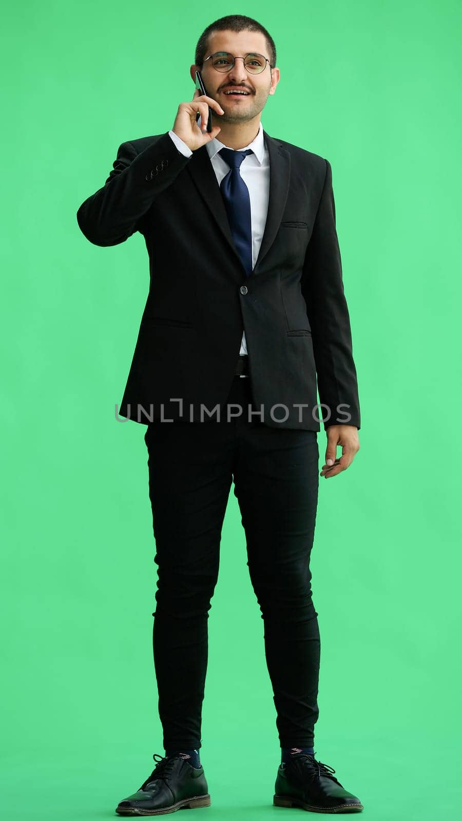 young man in full growth. isolated on green background speaks on the phone by Prosto