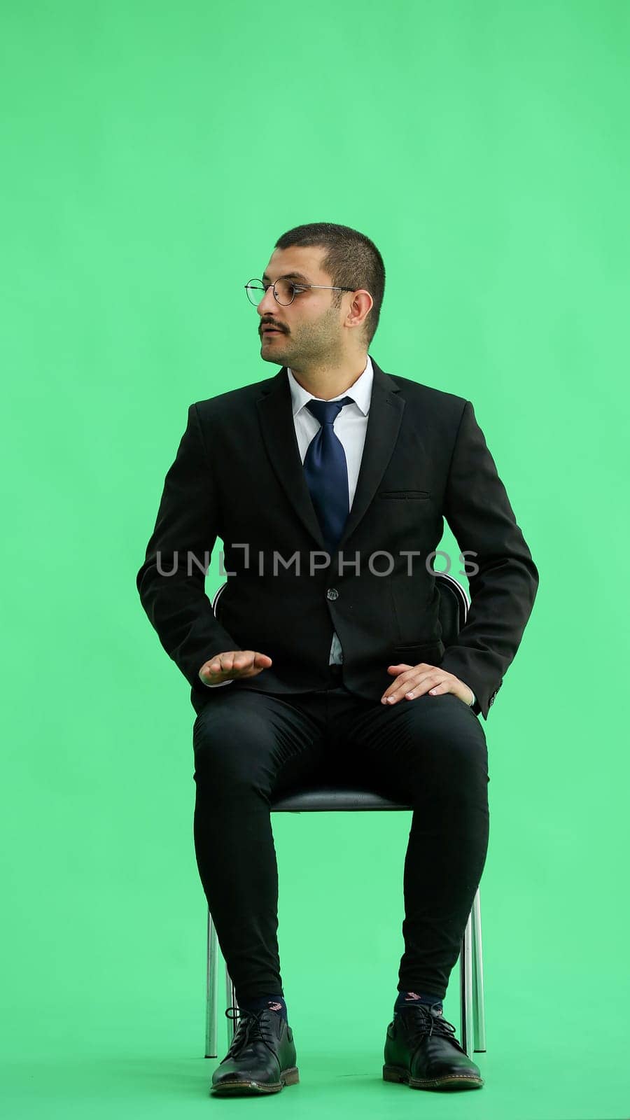 young man in full growth. isolated on a green background sitting on a chair by Prosto