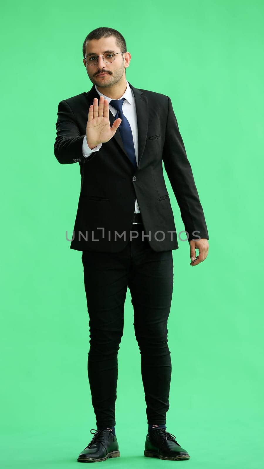 man in full growth. isolated on green background shows stop sign with hand.