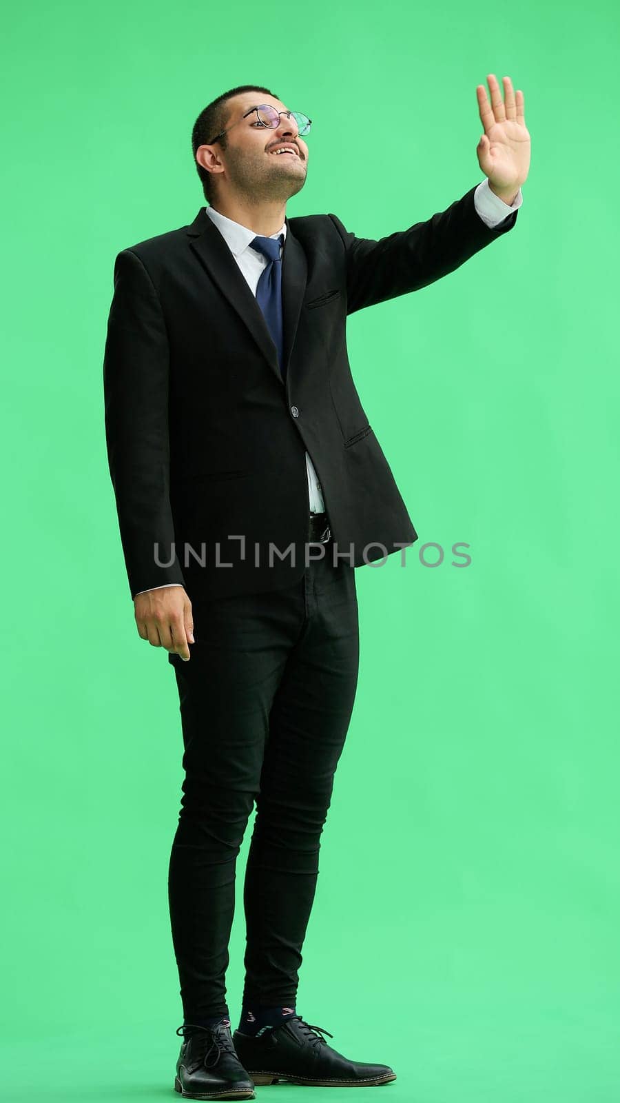 young man in full growth. isolated on green background shows hello with hand by Prosto