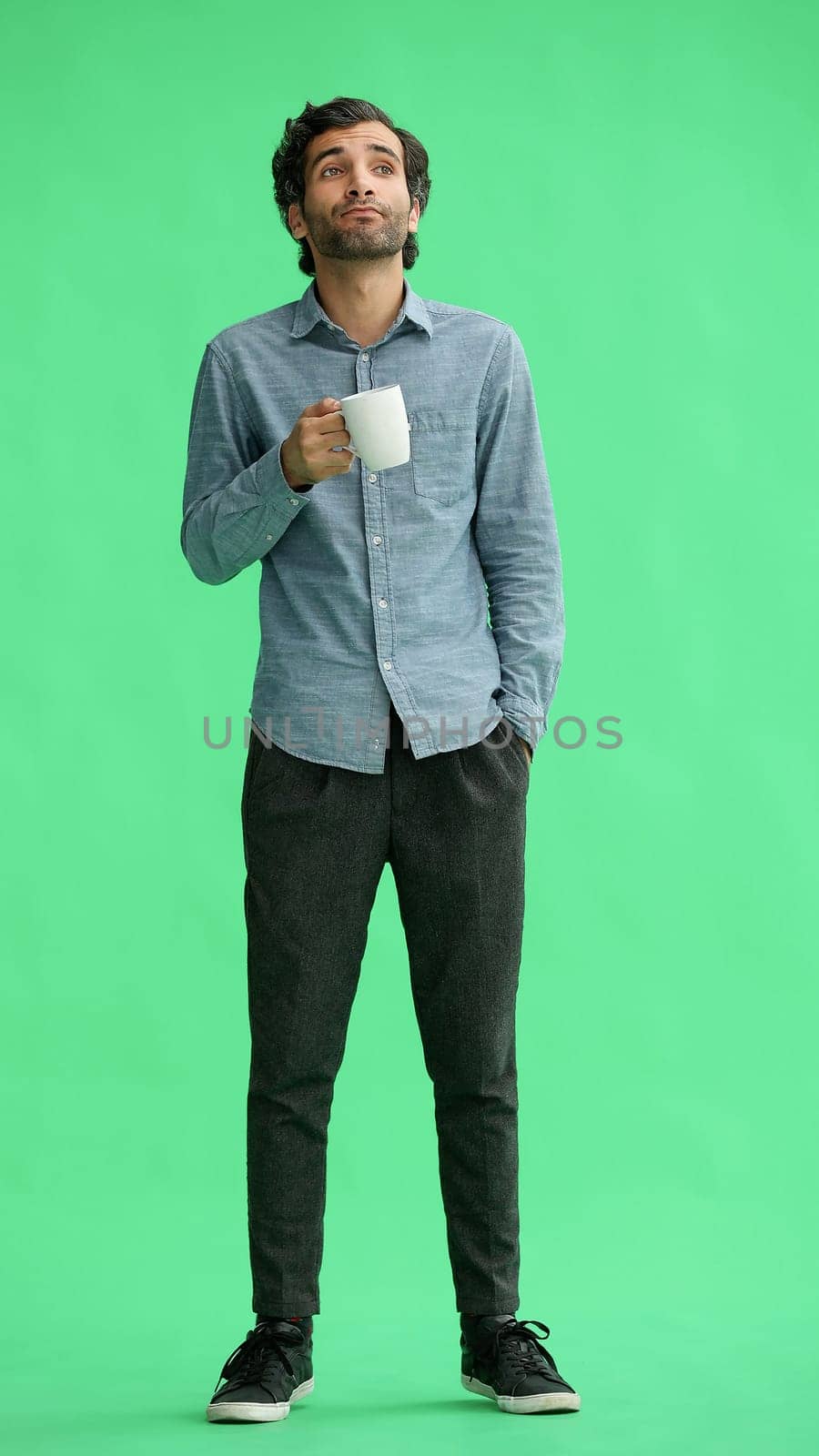 young man in full growth. isolated on green background. holding a mug of coffee.