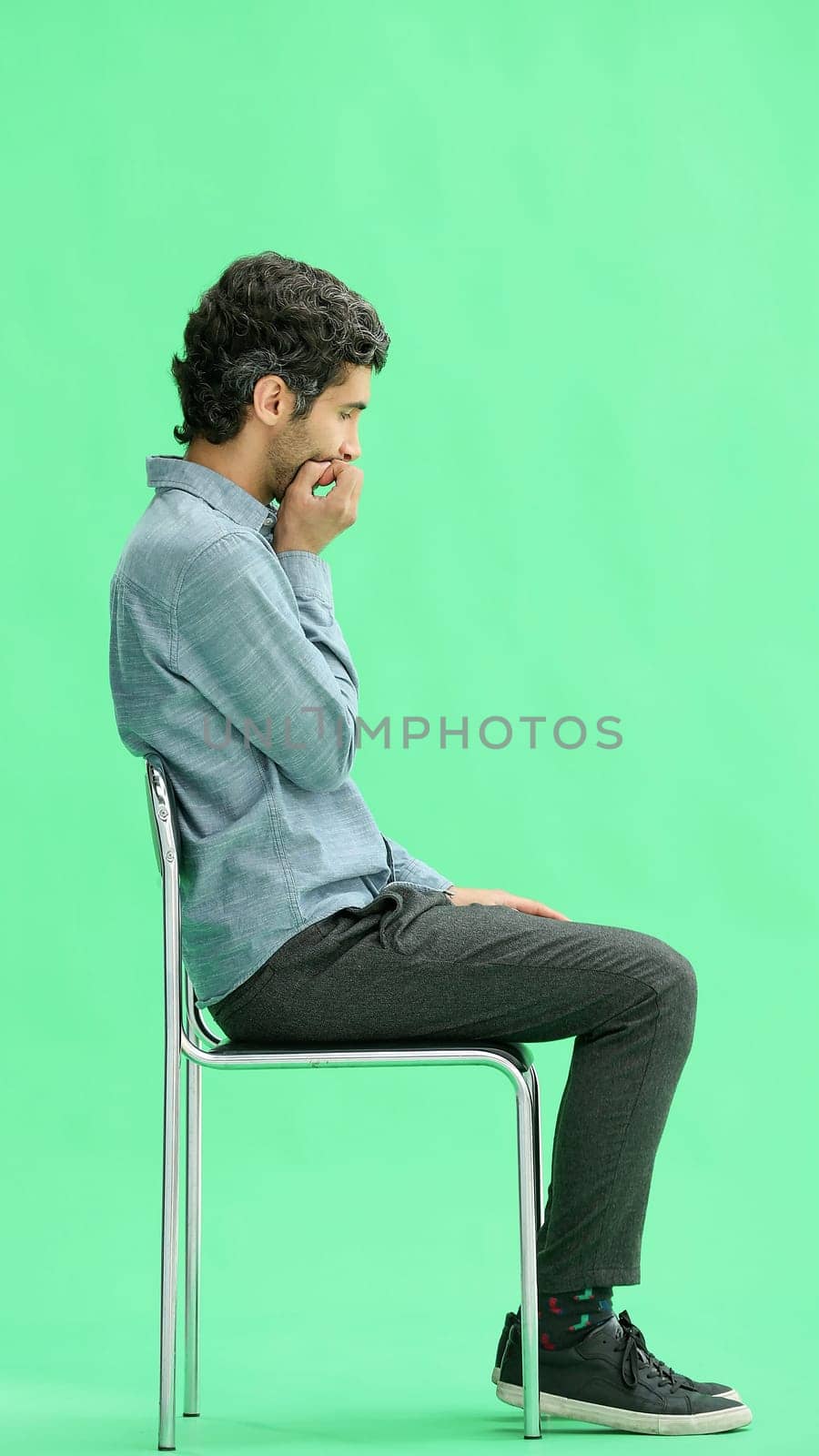 young man in full growth. isolated on a green background sitting on a chair.