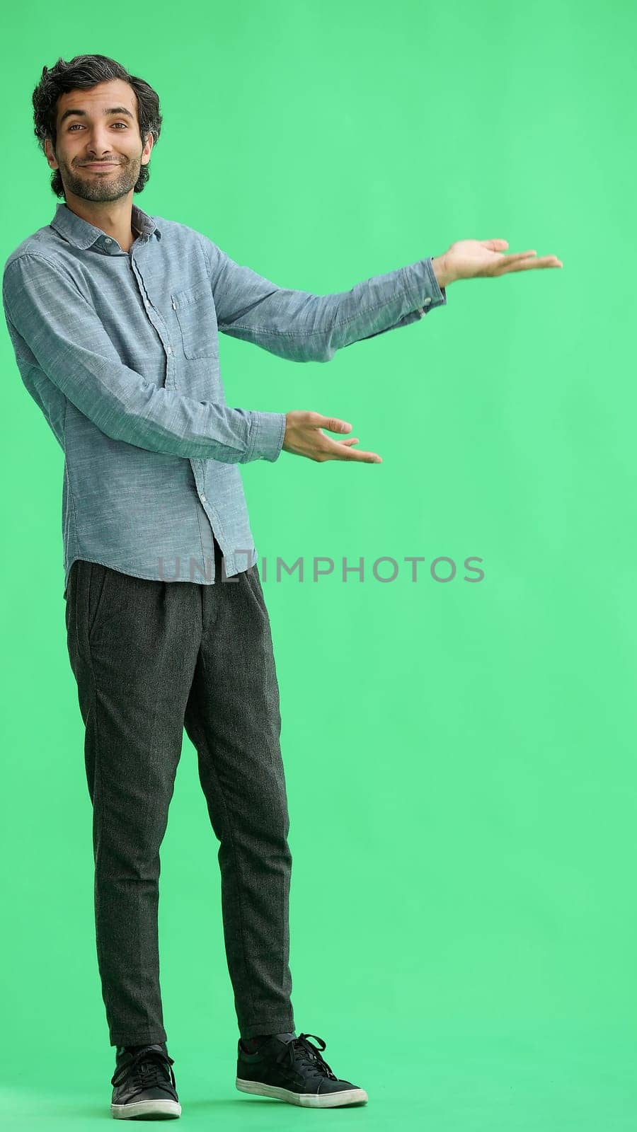 young man in full growth. isolated on green background demonstrates with hands by Prosto