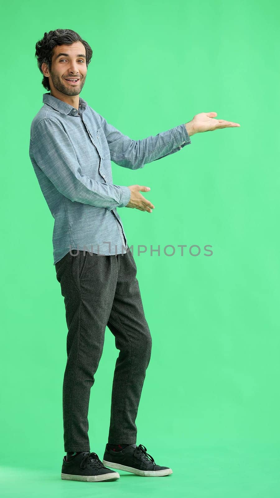 young man in full growth. isolated on green background demonstrates with hands by Prosto