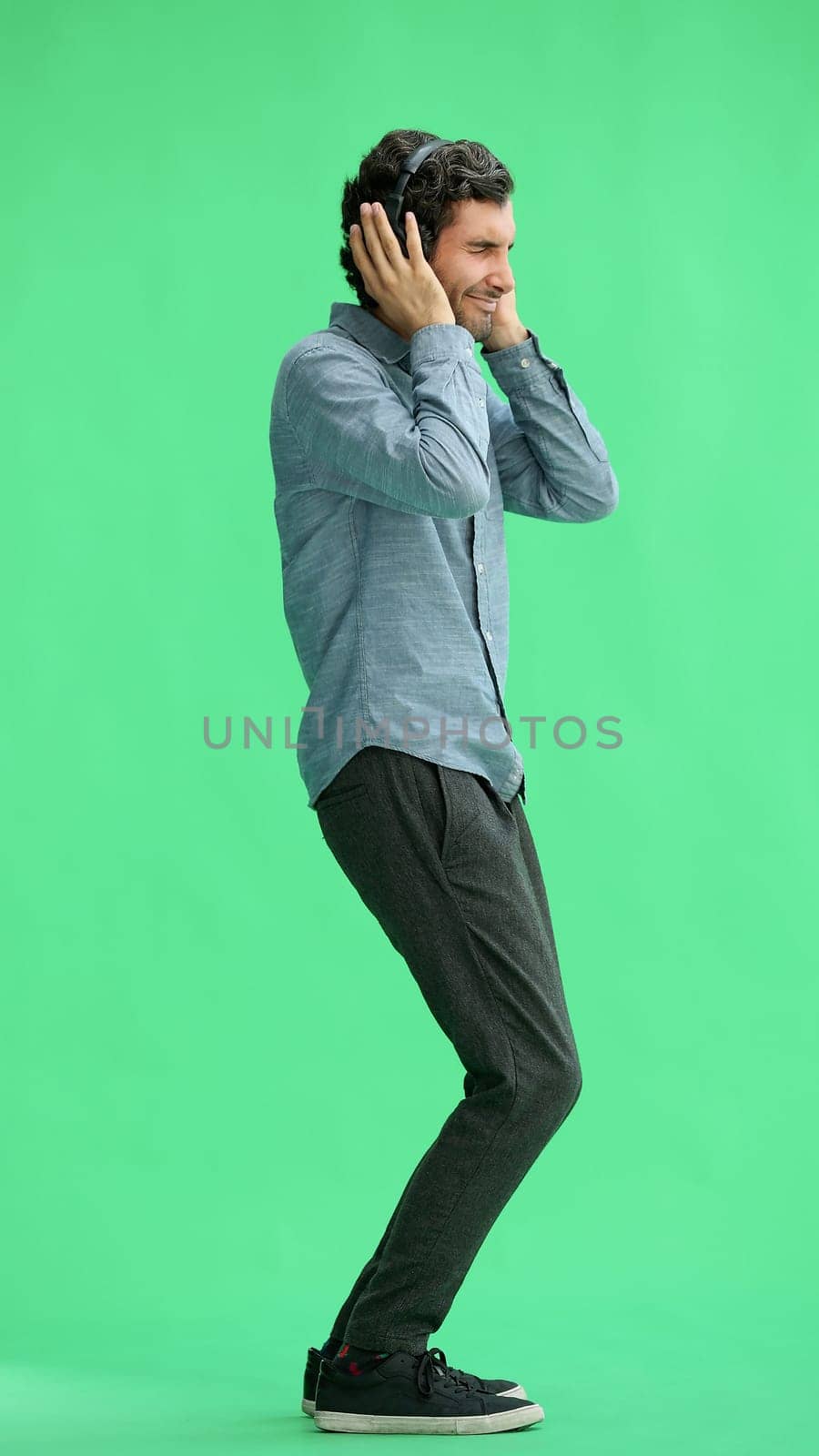 man in full growth. isolated on green background wearing headphones dancing.