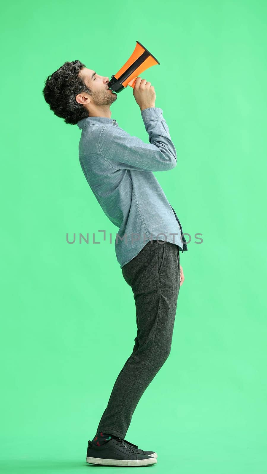 man isolated on a green background in business clothes with a loudspeaker in his hand by Prosto