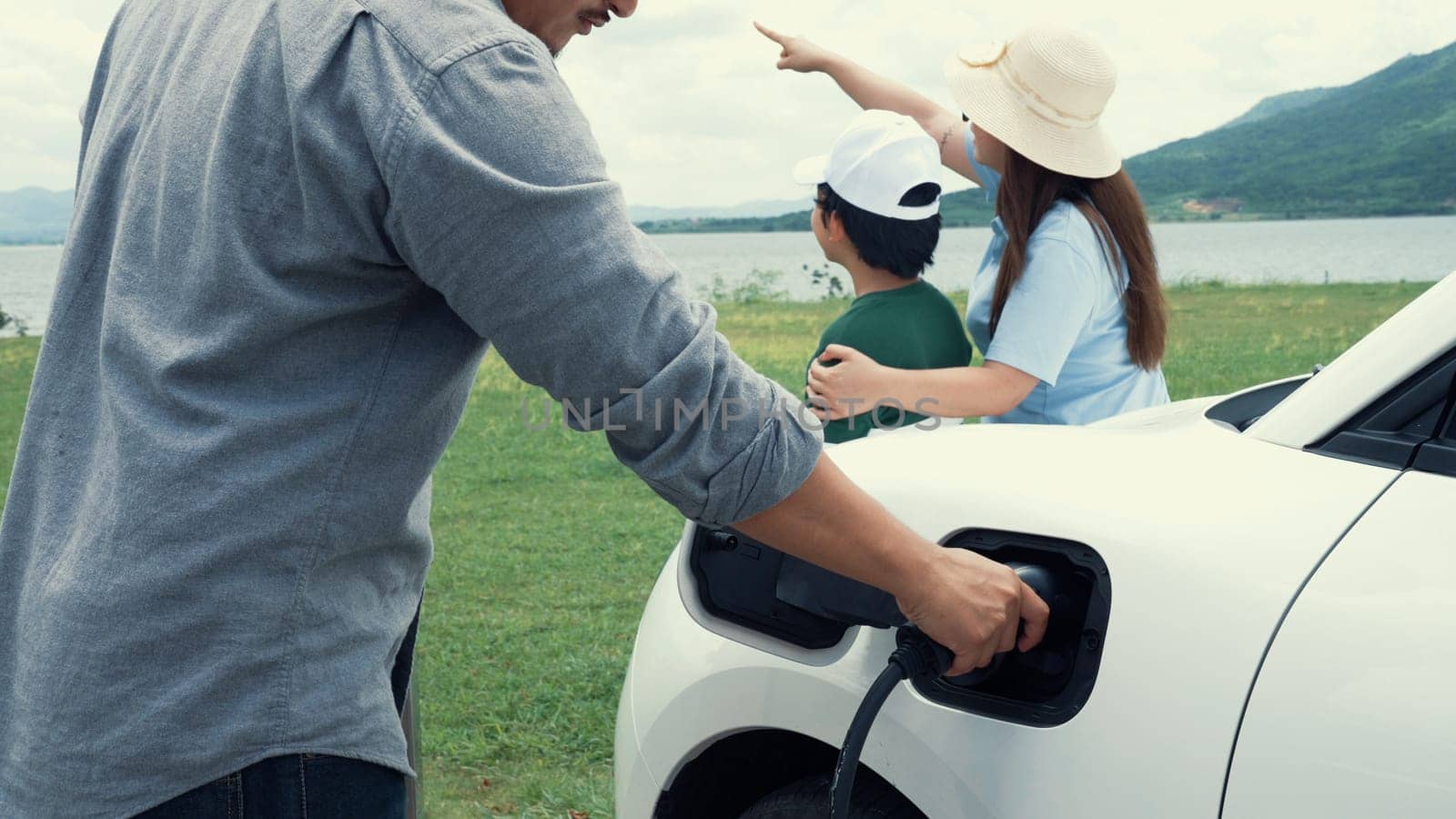 Concept of progressive happy family enjoying their time at wind farm with electric vehicle. Electric vehicle driven by clean renewable energy from wind turbine generator for charging station.