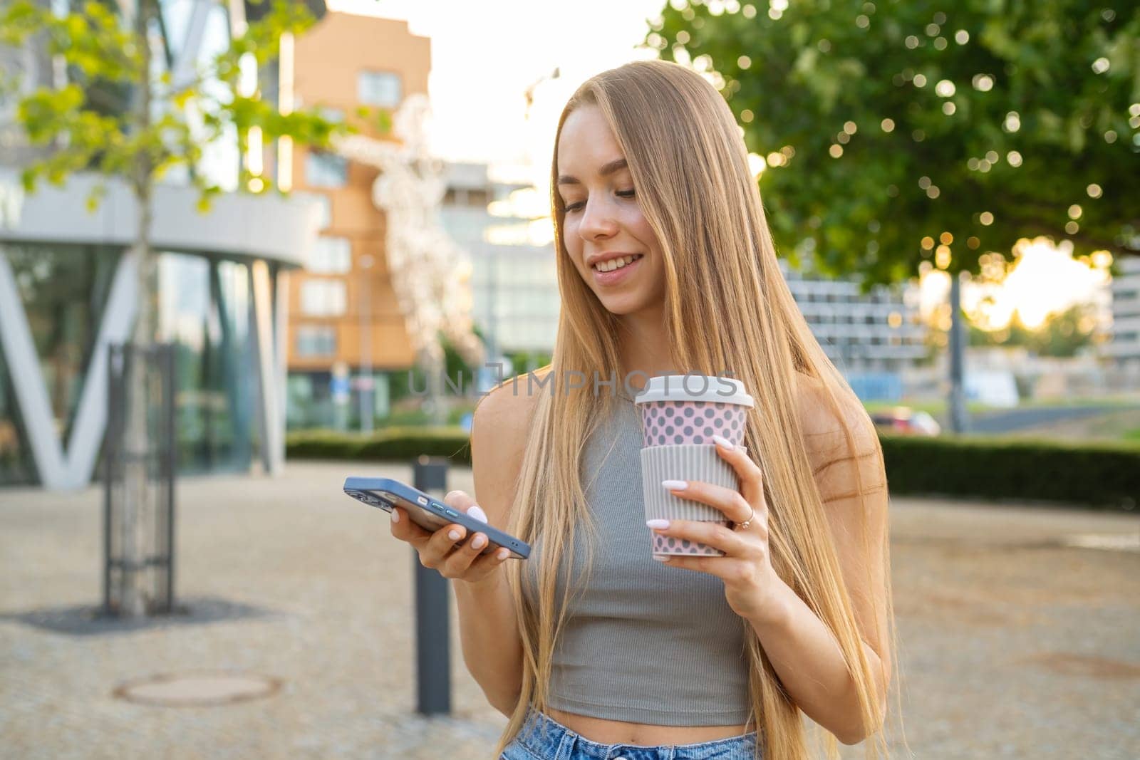 Young blonde hair woman testing to her friends, standing in the street with cup of coffee.