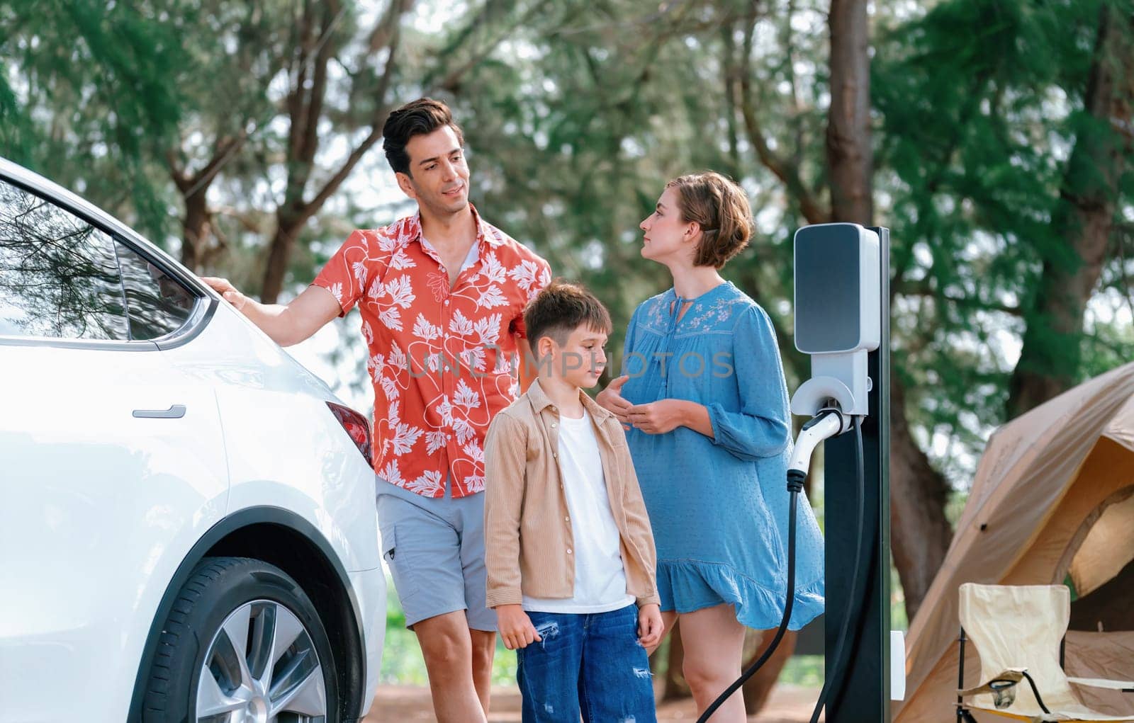 Outdoor adventure and family vacation camping in nature travel by eco friendly car for sustainable future. Lovely family recharge EV car with EV charging station in campsite. Perpetual