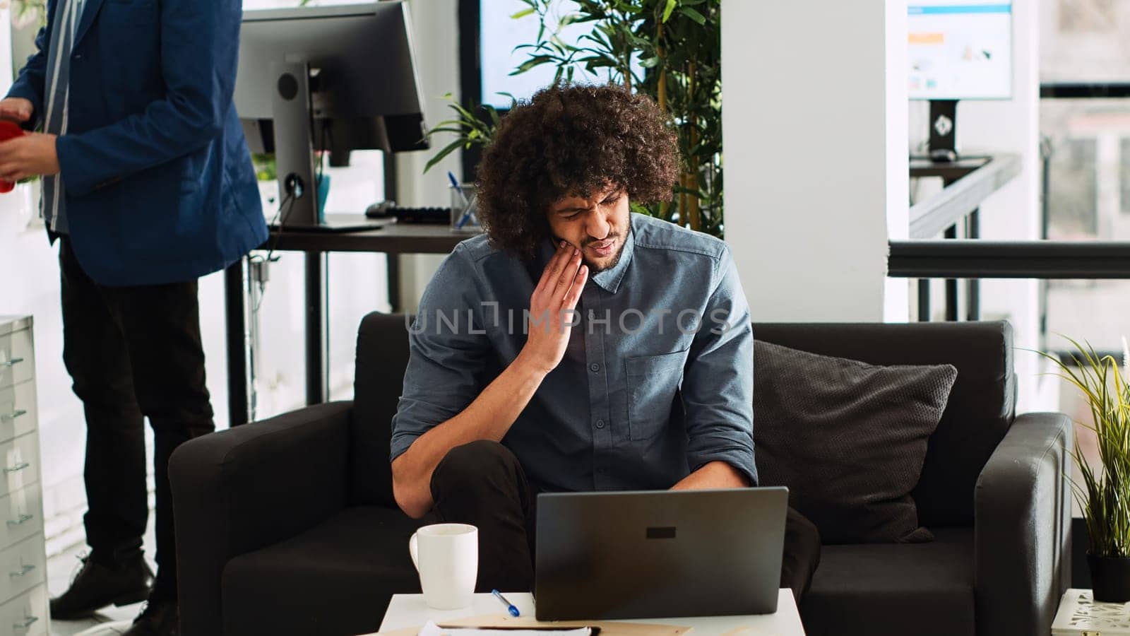 Dental inflammation in business office. Company employee suffering from toothache, cavity infection at work. Middle eastern man with caries feeling unwell in startup open space.