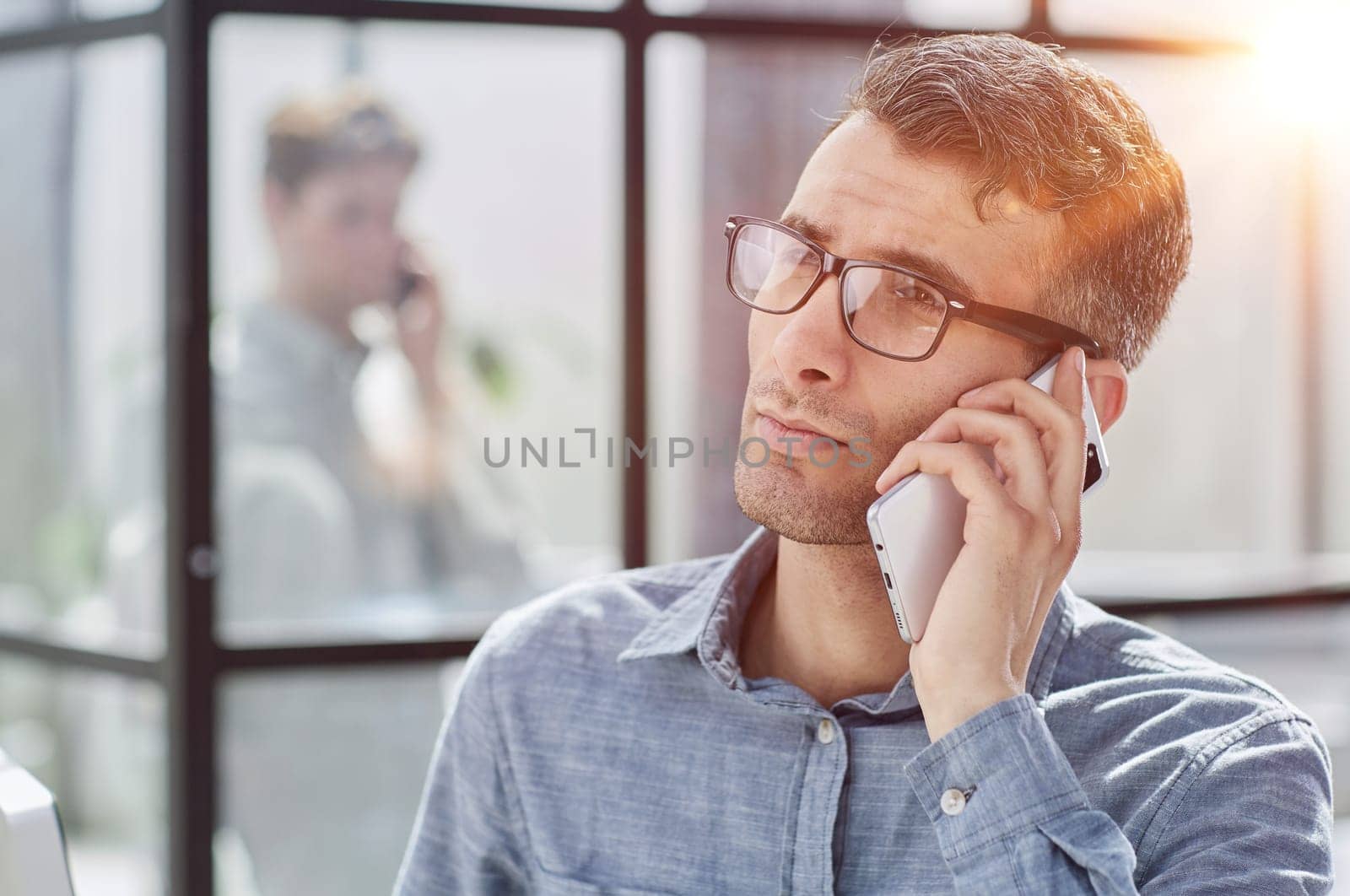 young man in a blue shirt talking on the phone in the office