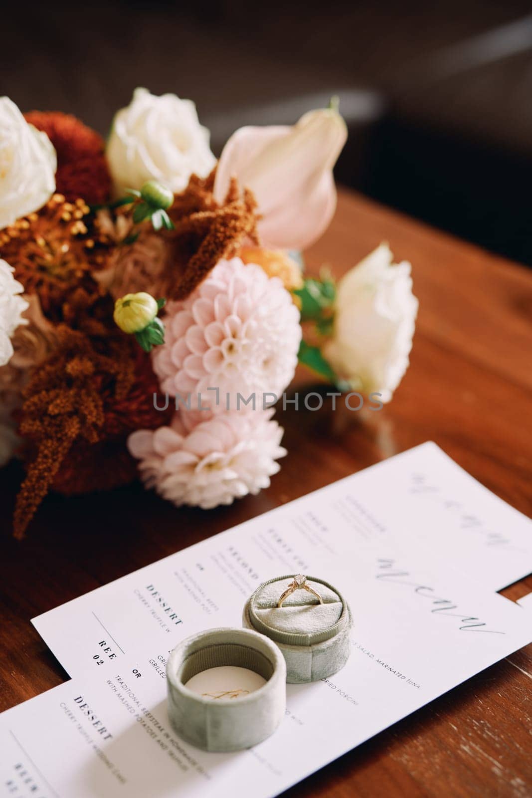 Engagement ring in a box stands on a festive menu on a wooden table near a bouquet by Nadtochiy