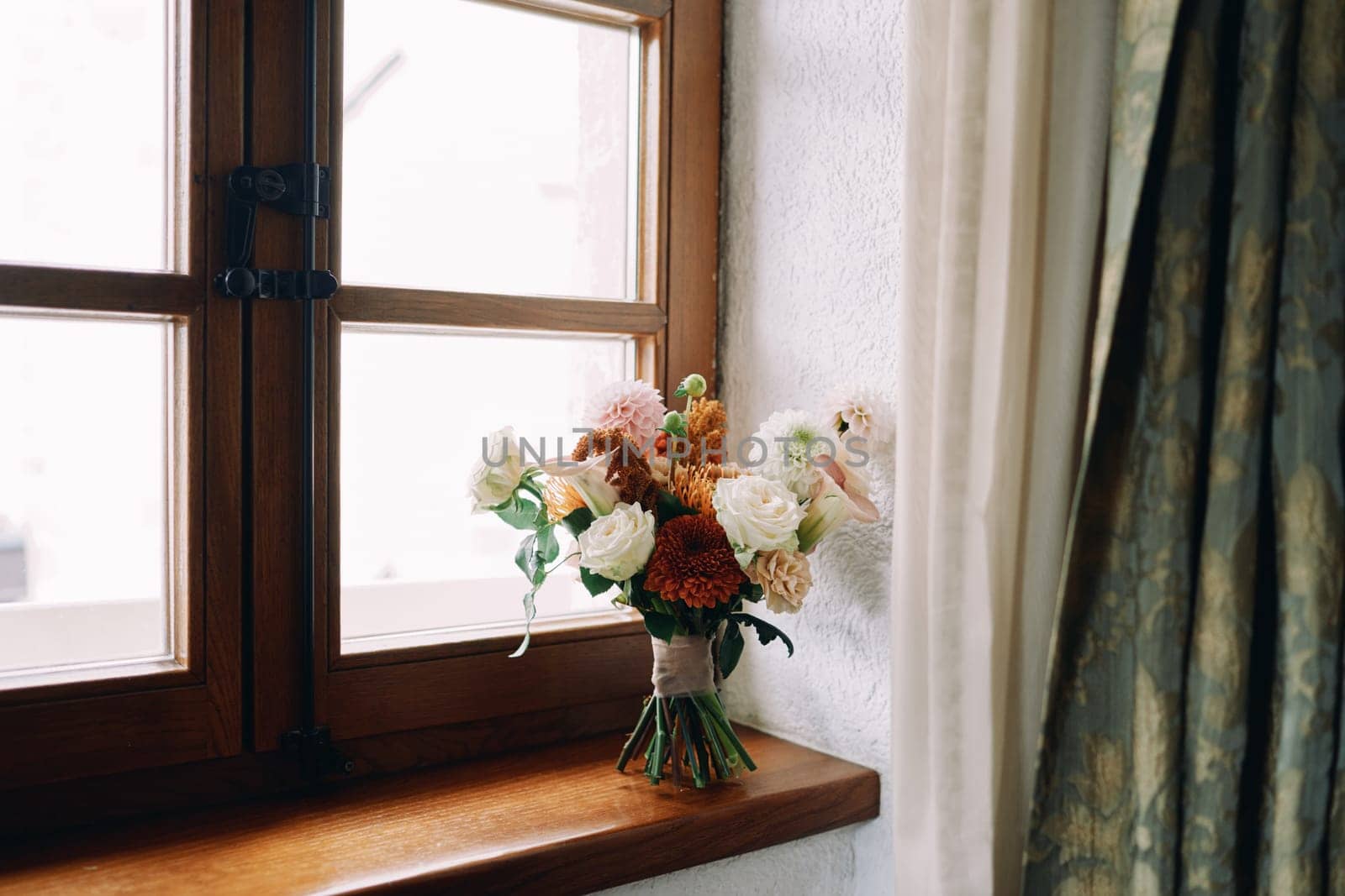 Bride bouquet stands on a wooden windowsill near the curtains by Nadtochiy