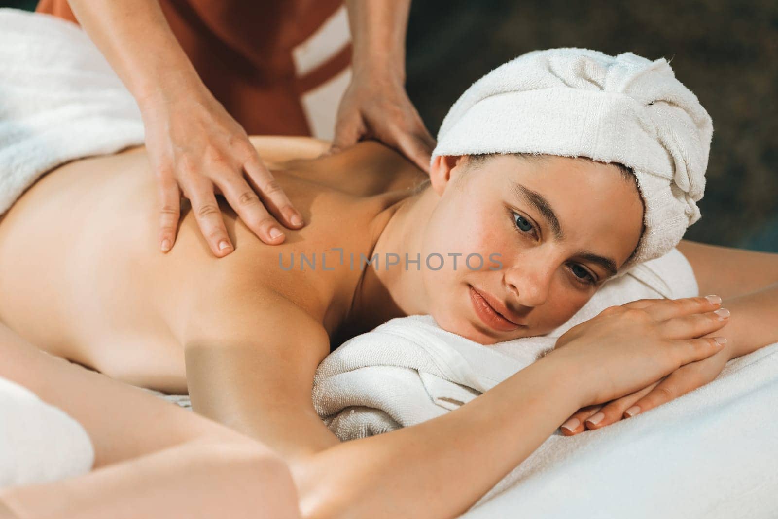 Beautiful young woman received a back massage on a spa bed from professional masseuse. Attractive female relaxes deeply by skilled hands of the massage therapist. Surrounded with nature. Tranquility.