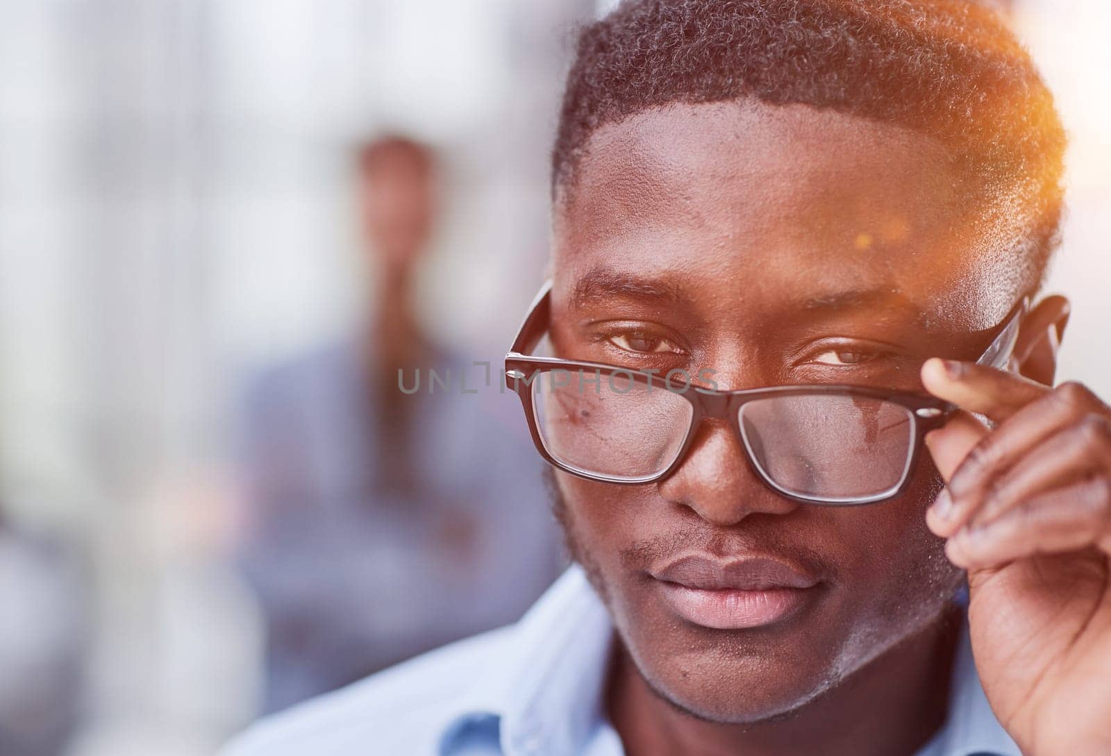 a black man in a blue shirt adjusts his glasses. Against the backdrop of the office